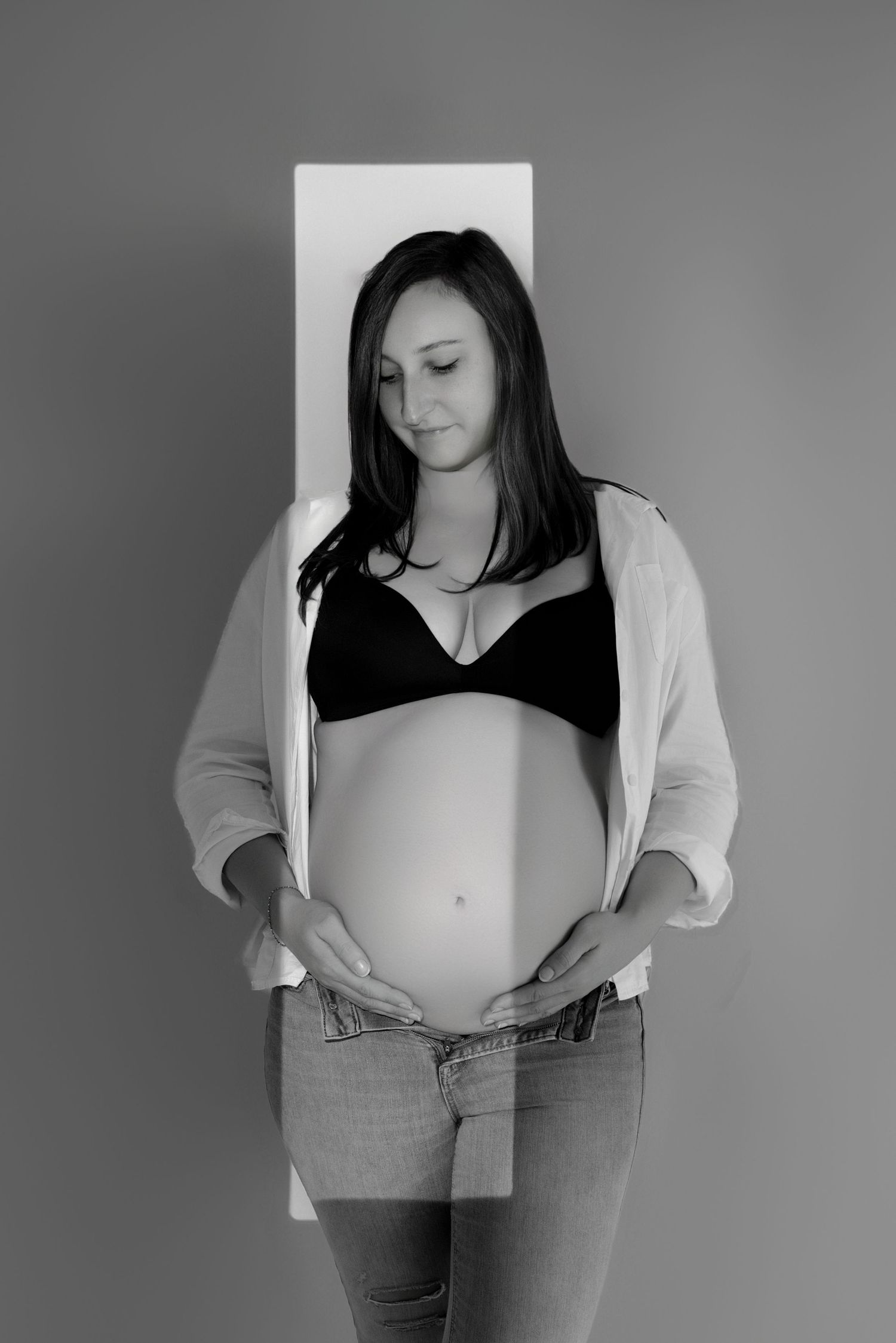 Portrait intimiste en noir et blanc d'une femme enceinte, mains sur son ventre rond, séance photo de grossesse par Cindy Poulet Photographe