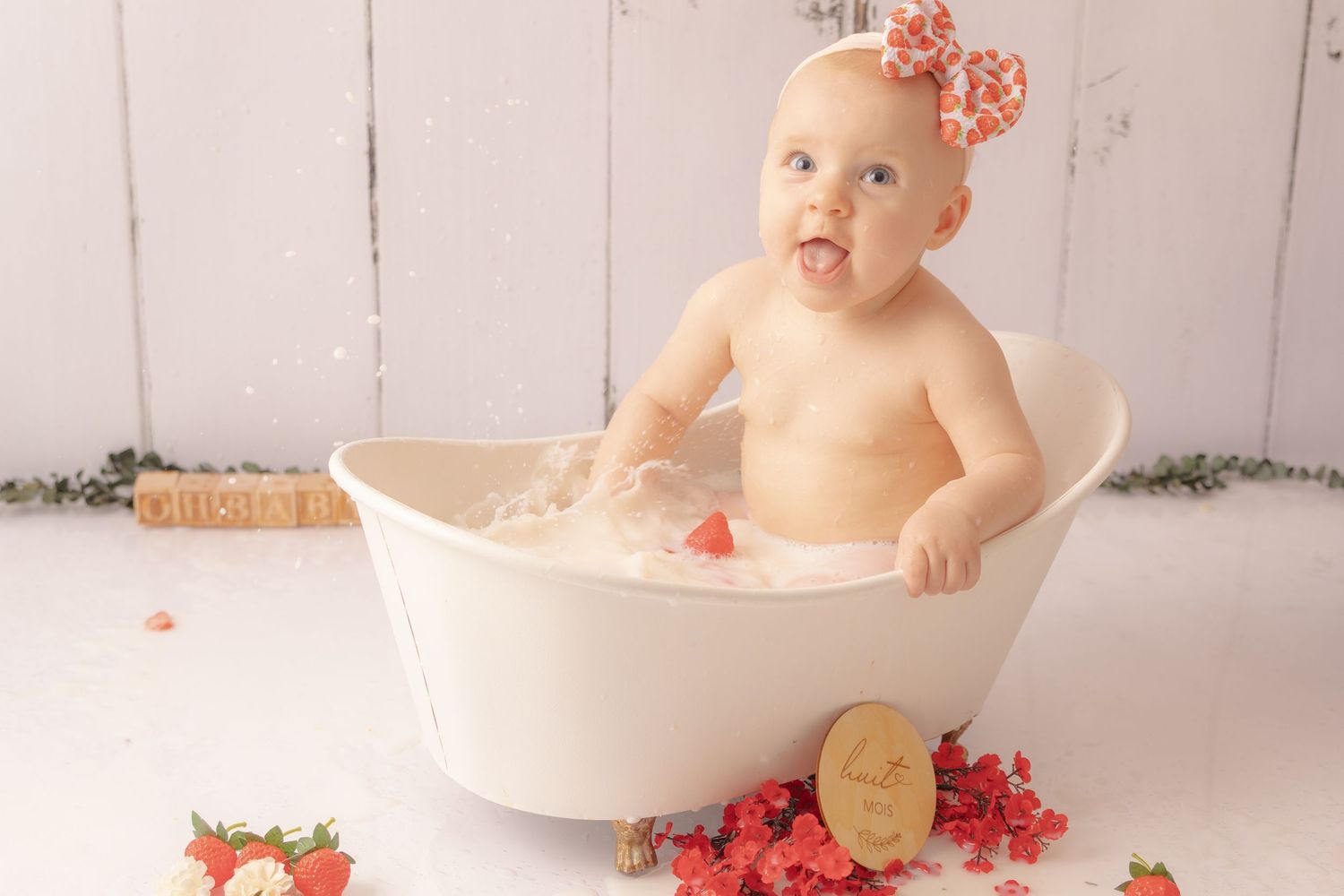 Séance photo bébé bain de lait par Cindy Poulet Photographe : enfant souriant dans une petite baignoire blanche, thème fraise.