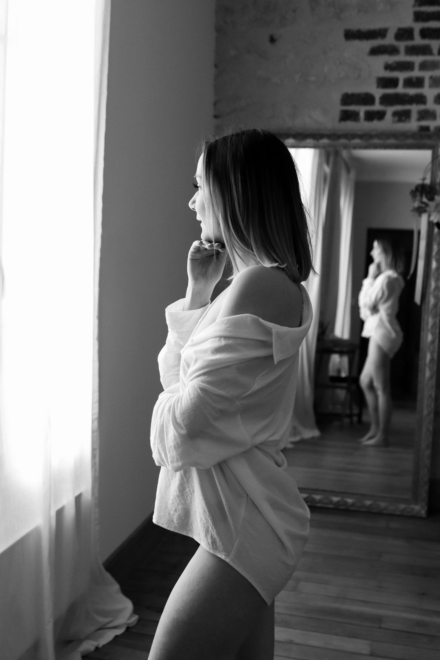 Femme en chemise blanche de profil devant un miroir, séance boudoir