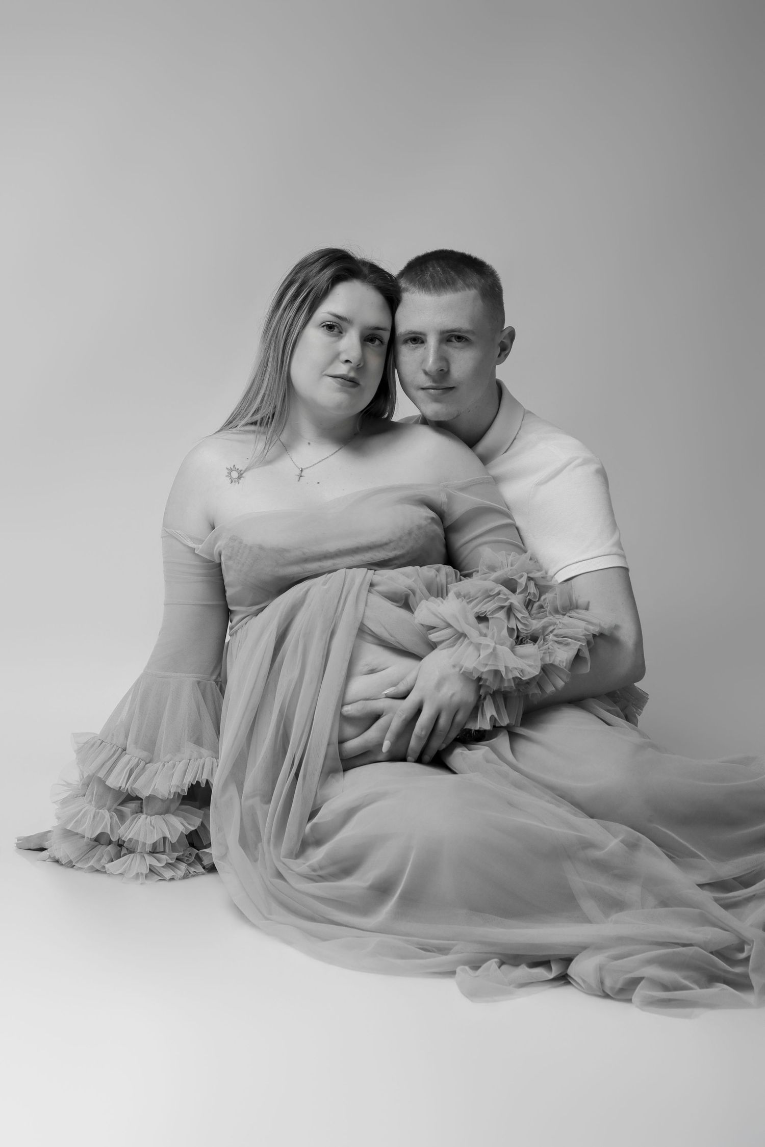 Séance photo de grossesse artistique en studio : femme enceinte de profil allongée et drapée dans un voile rose vaporeux, par Cindy Poulet P