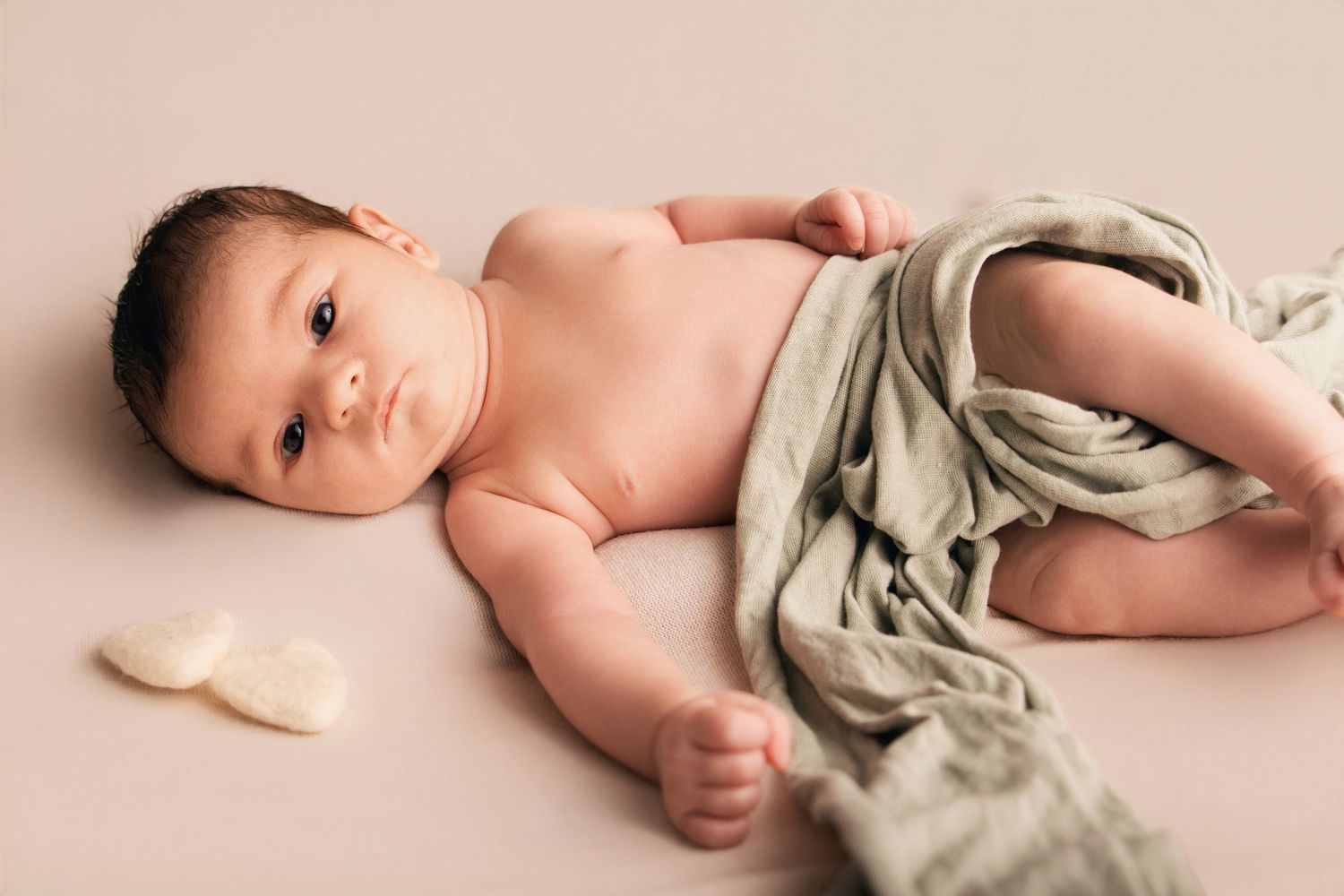 Séance naissance par Cindy Poulet Photographe : bébé avec lange vert sauge et petits cœurs, portrait studio minimaliste.