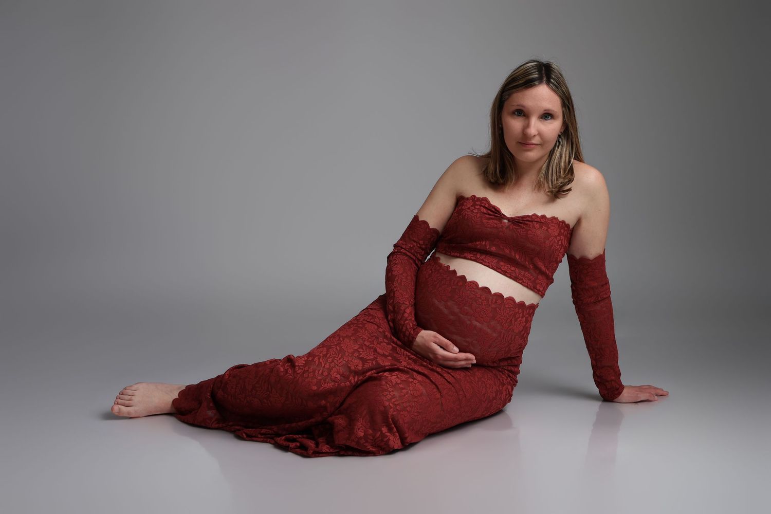 Femme enceinte en tenue rouge allongée gracieusement, séance photo grossesse