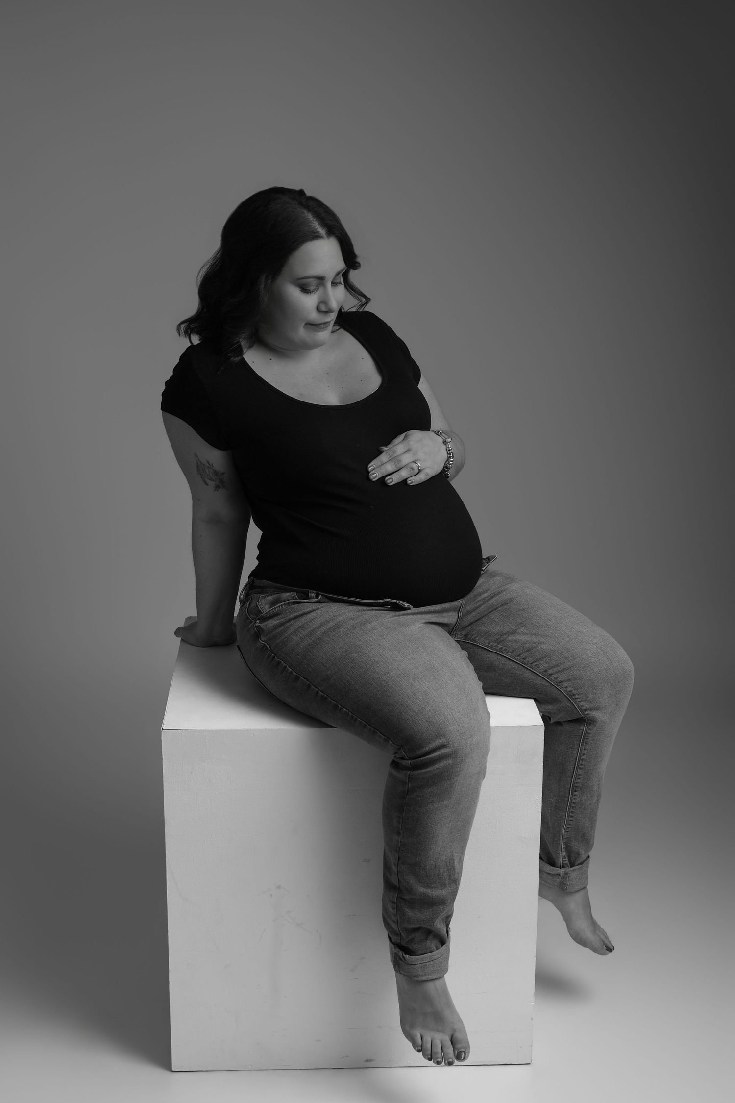 Femme enceinte assise sur un cube en tenue décontractée, portrait grossesse en noir et blanc