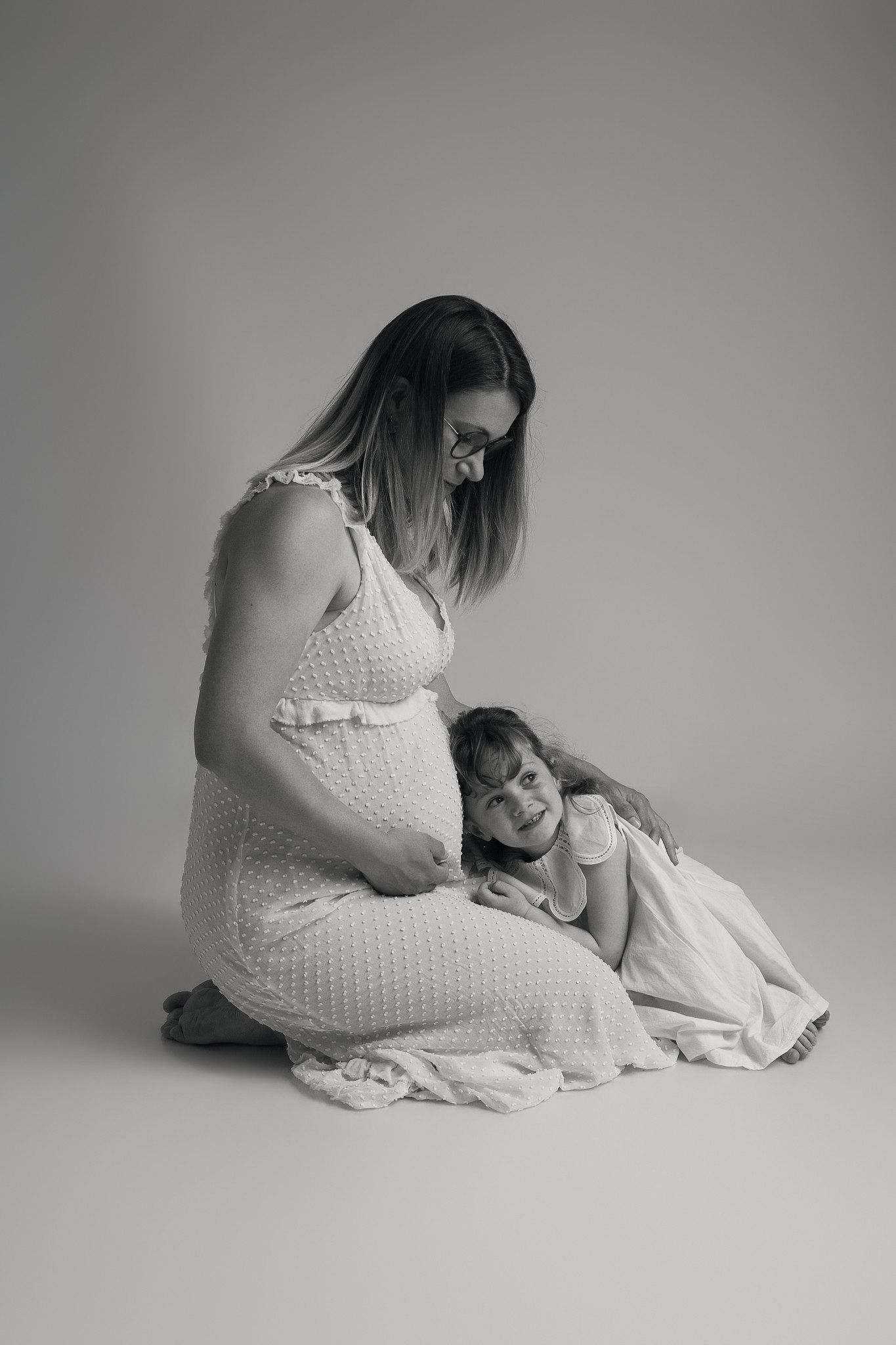 Petite fille embrassant le ventre de sa maman enceinte en studio, shooting photo maternité et famille par Cindy Poulet Photographe