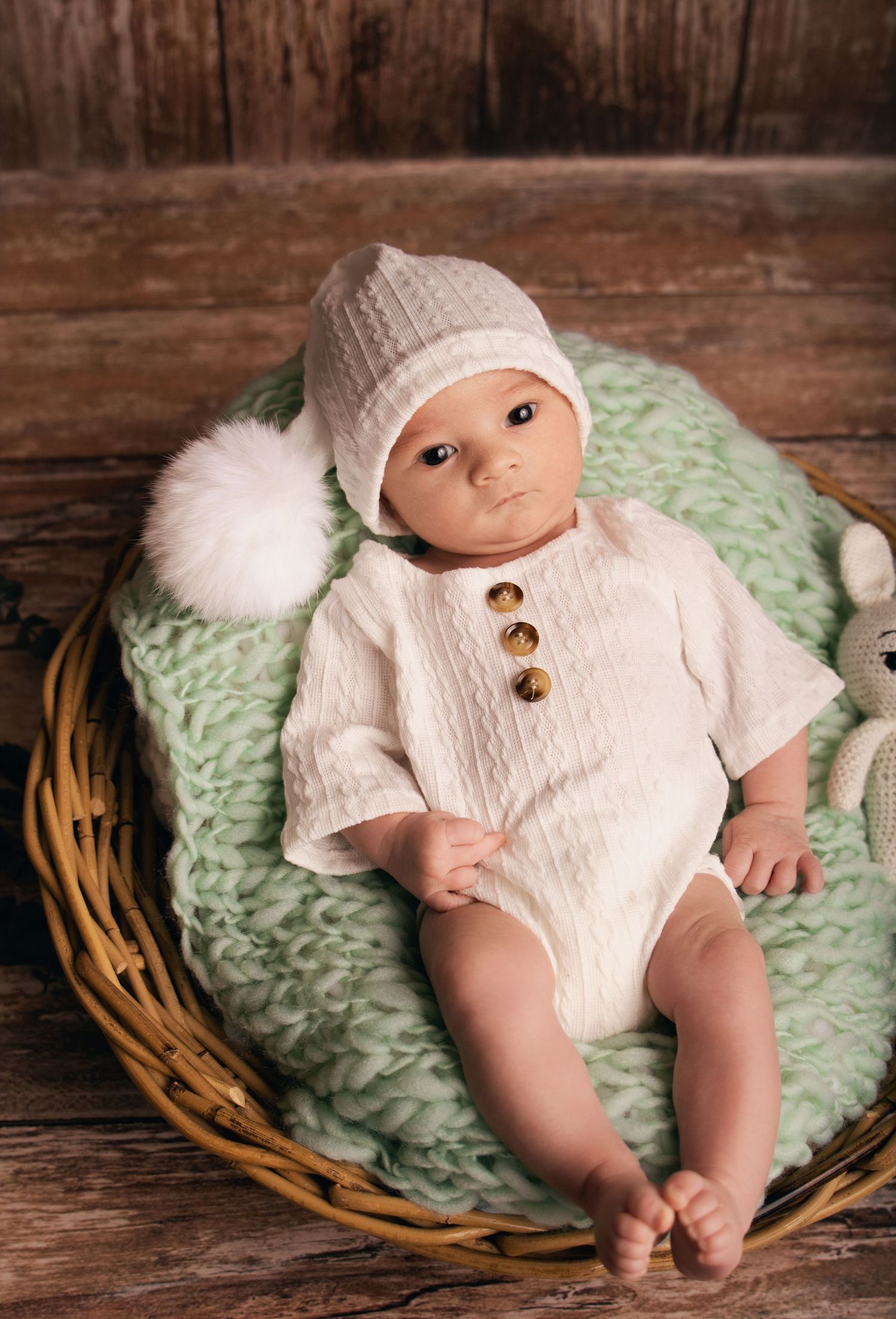 Photographie de nouveau-né par Cindy Poulet Photographe : bébé vêtu d'une tenue tricotée blanche avec bonnet à pompon.