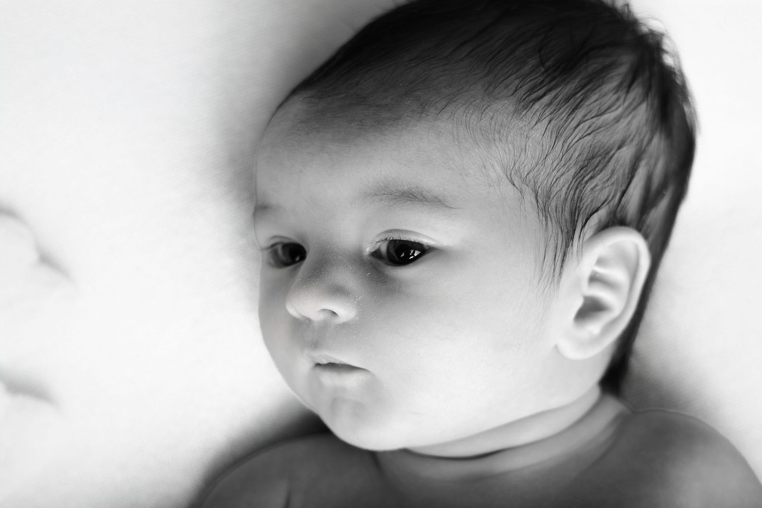 Portrait de naissance en noir et blanc par Cindy Poulet Photographe : gros plan artistique sur le visage d'un nouveau-né au regard calme et