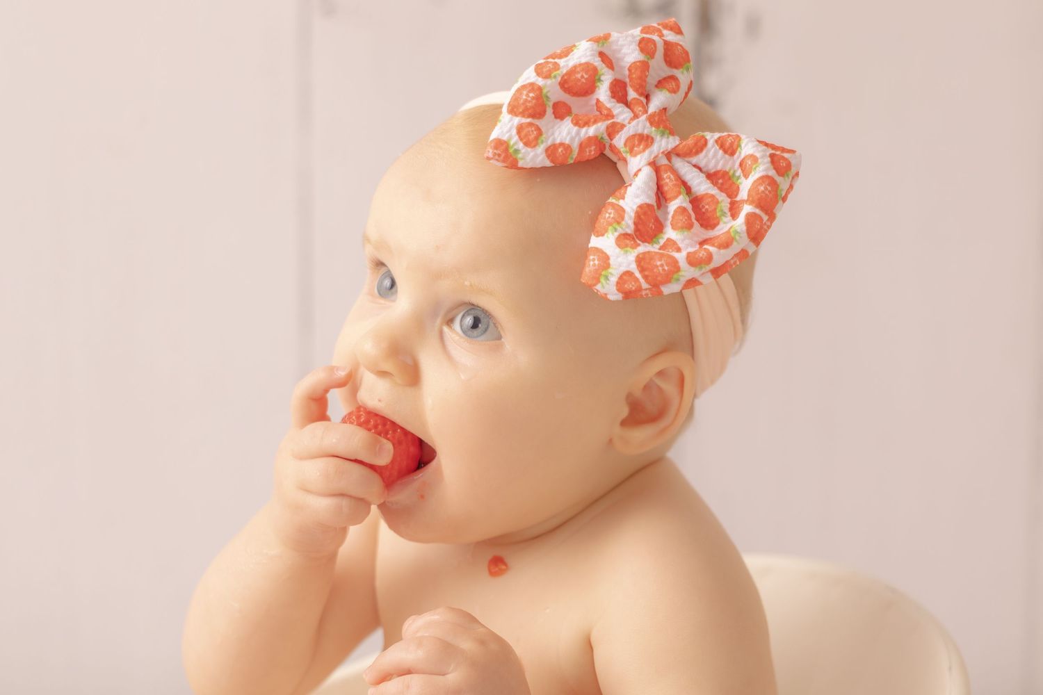 Séance photo bébé thématique par Cindy Poulet Photographe : portrait d'un enfant avec un bandeau à nœud fraise croquant une fraise.
