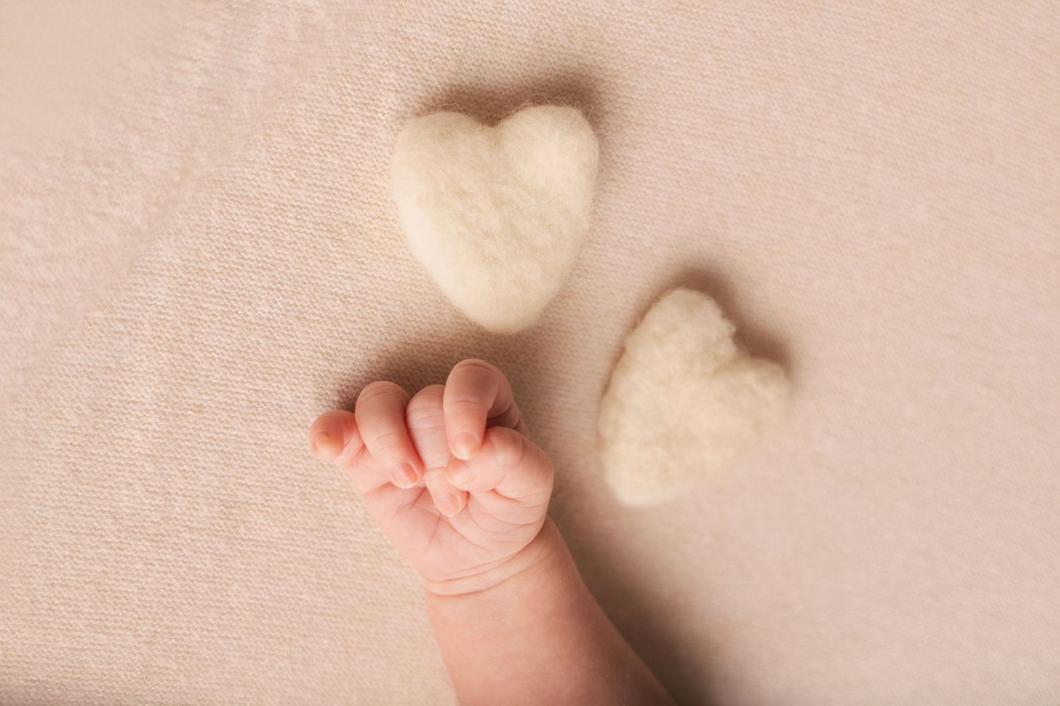 Détail de séance photo nouveau-né par Cindy Poulet Photographe : gros plan sur la main d'un bébé à côté de deux petits cœurs en laine.