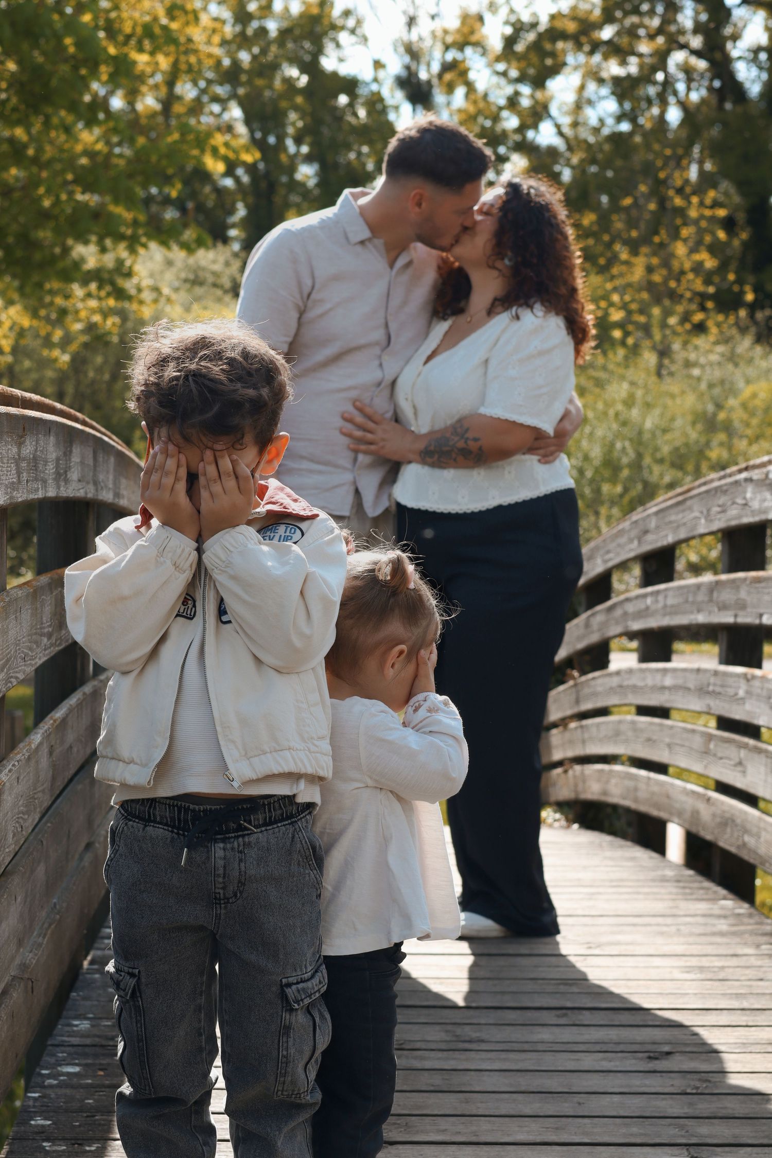 Séance photo famille avec parents embrassant et enfants jouant sur un pont en bois