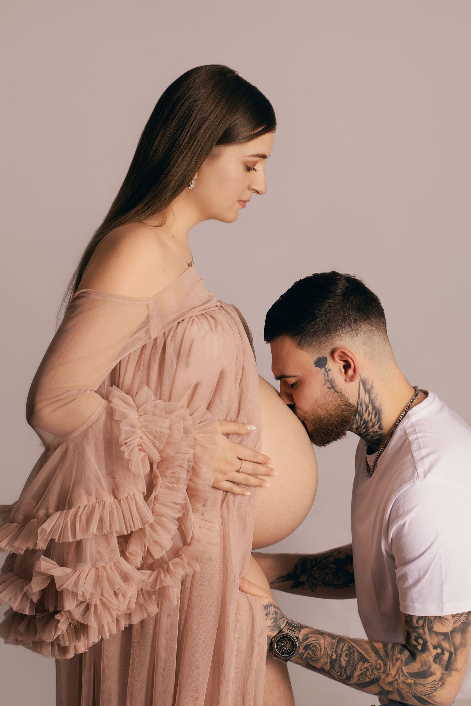 Futur papa embrassant tendrement le ventre de la maman en studio. Séance grossesse émotion par Cindy Poulet à Septvaux, dans l'Aisne.