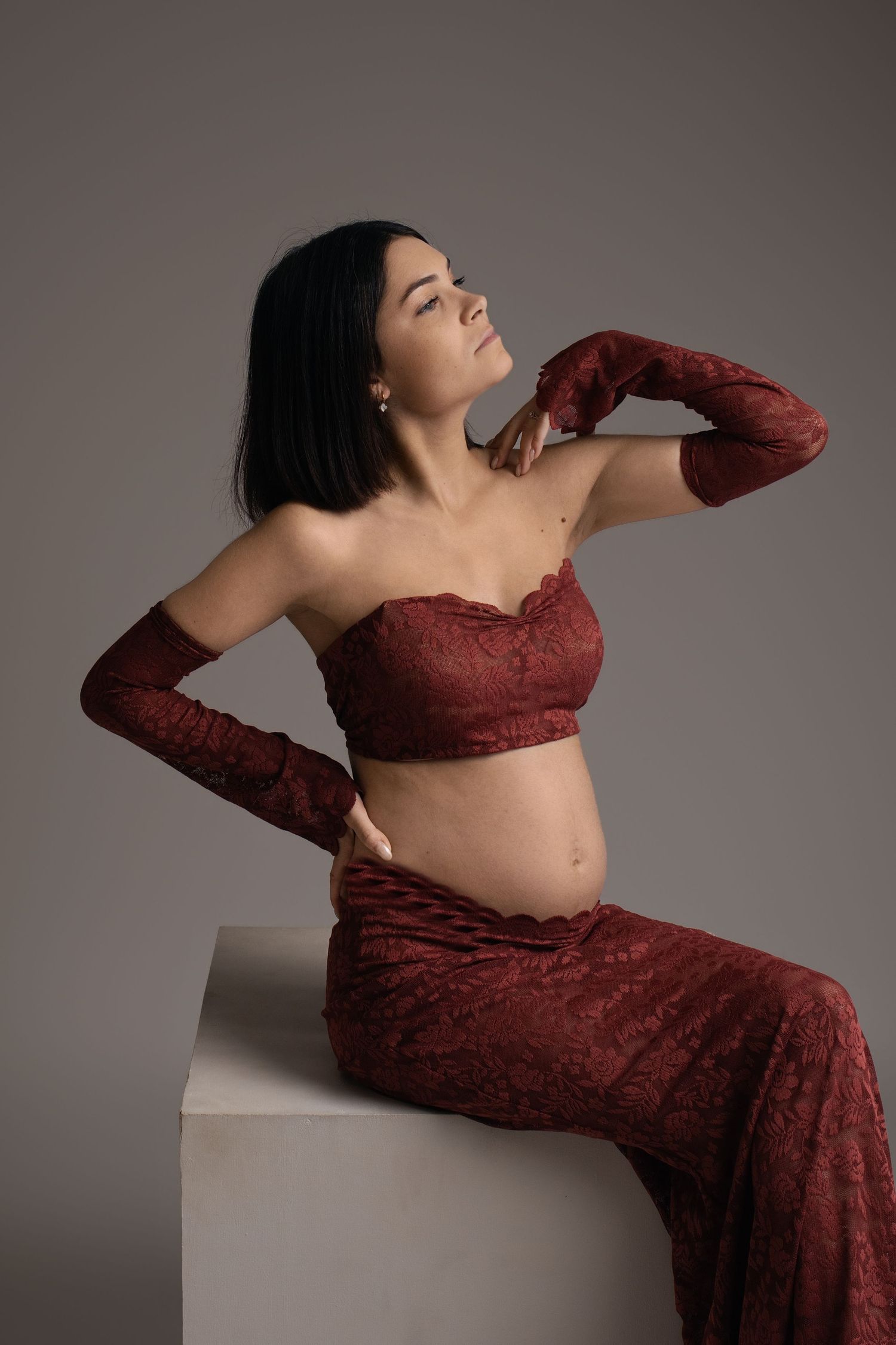 Femme enceinte en rouge assise, séance photo maternité en studio - Cindy Poulet photographe