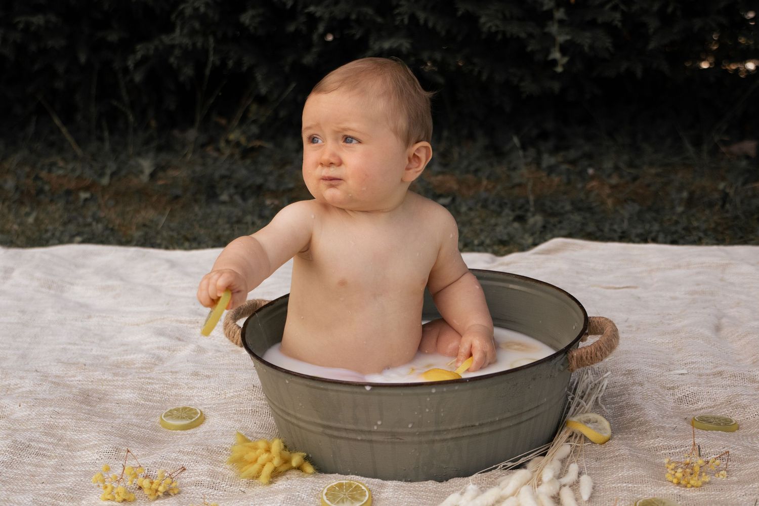 Séance photo bébé en extérieur par Cindy Poulet Photographe : un enfant dans une bassine en zinc pour un bain de lait décoré de citrons.