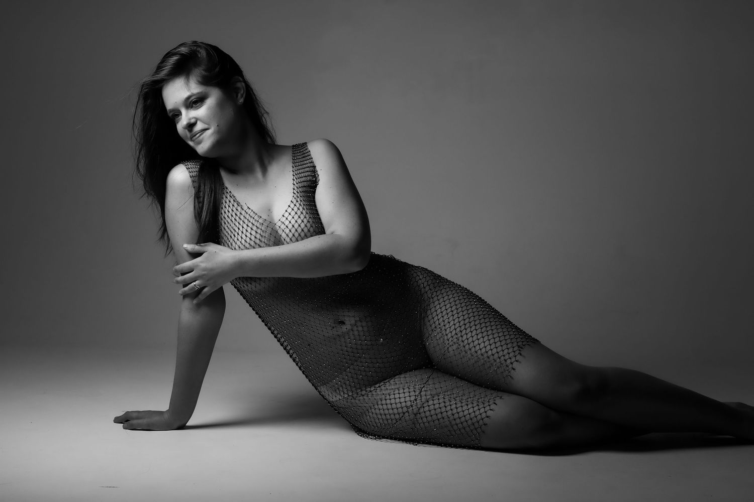 Portrait boudoir noir et blanc par Cindy Poulet Photographe : femme posant en studio dans une tenue résille artistique.