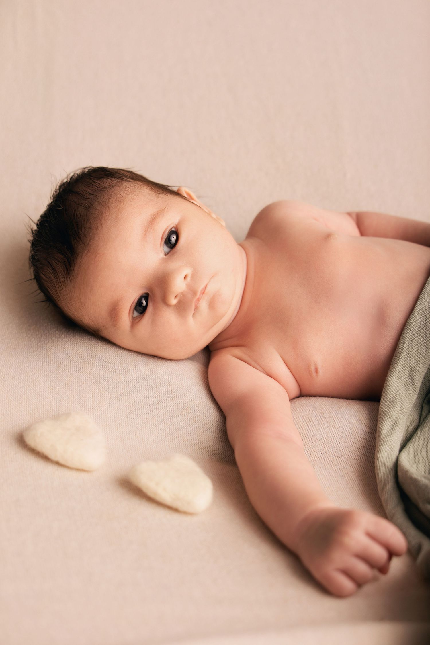 Nouveau-né éveillé allongé sur une couverture beige avec des petits cœurs, séance photo naissance en studio par Cindy Poulet Photographe
