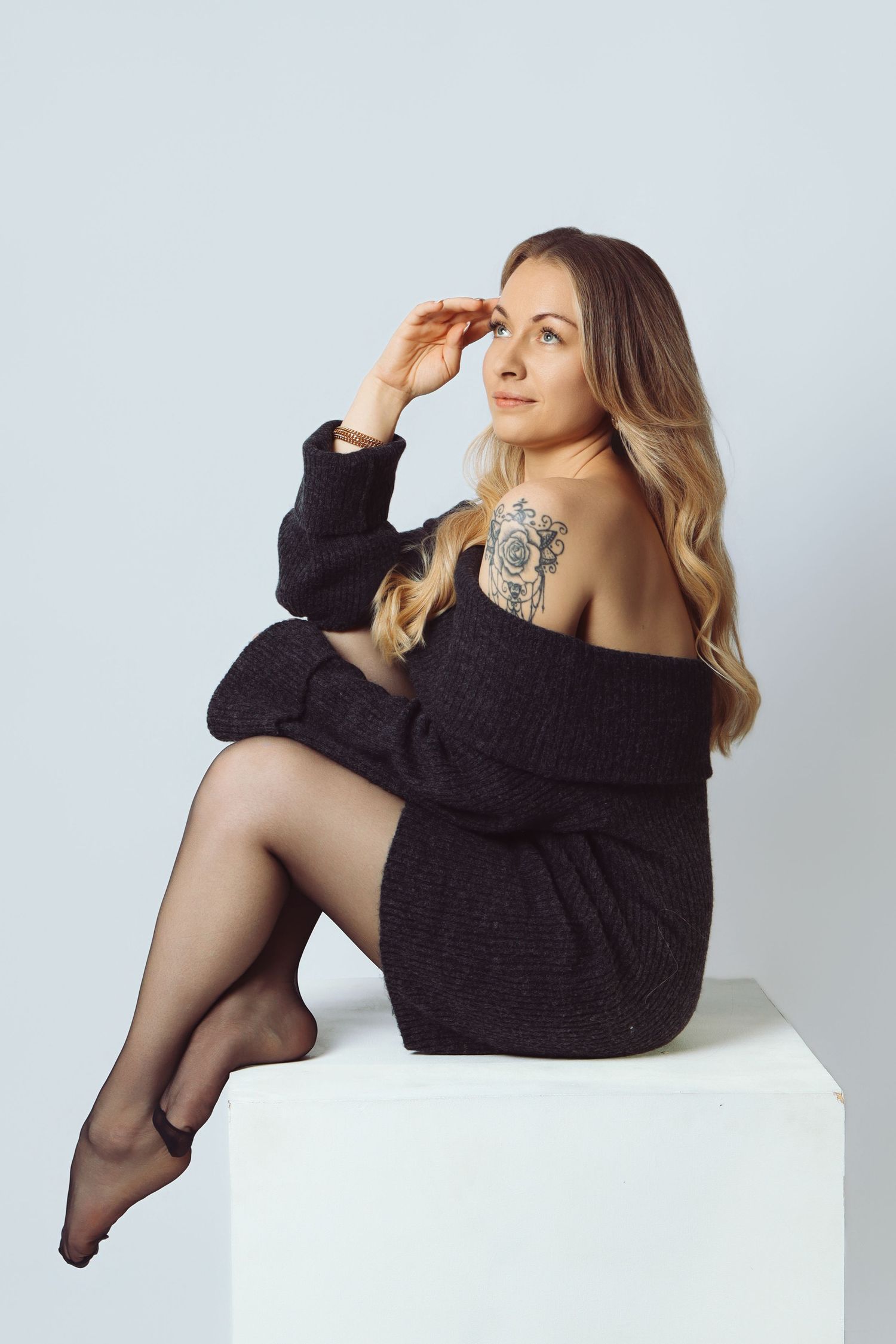 Portrait studio d'une femme tatouée en pull noir assise sur un cube, par Cindy Poulet Photographe proche Saint Quentin.