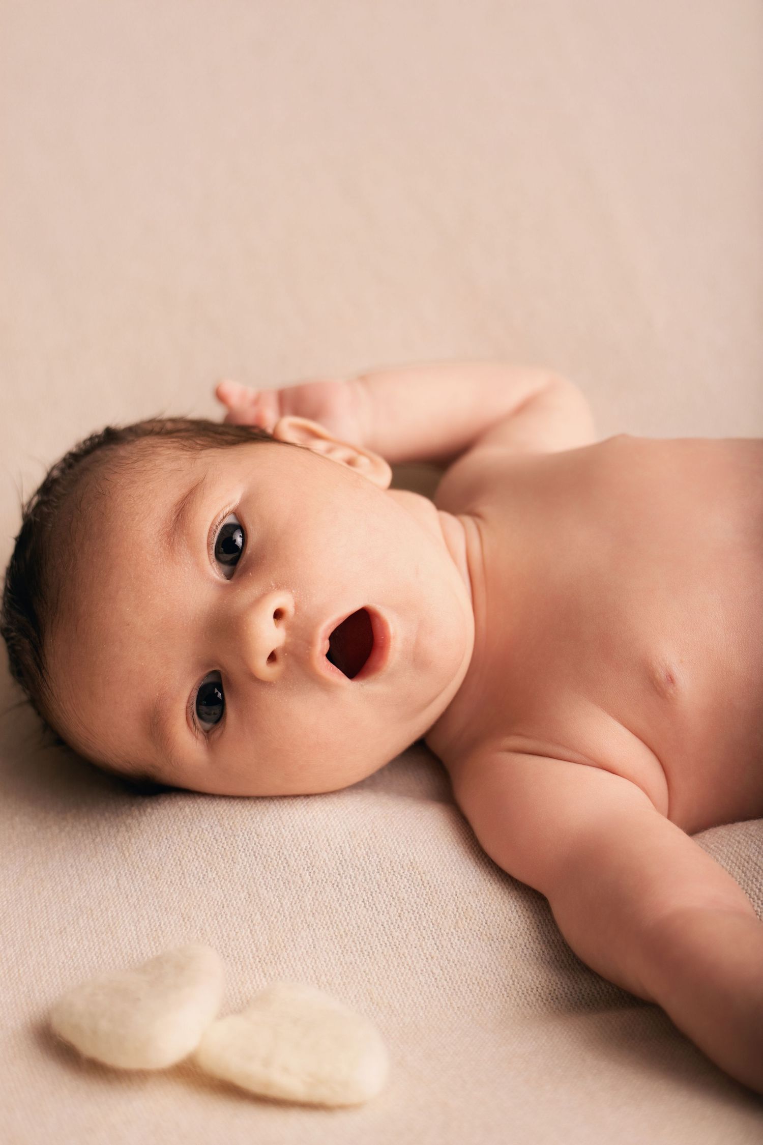 Portrait de nouveau-né expressif par Cindy Poulet Photographe : bébé capturé avec une expression naturelle sur un fond beige.