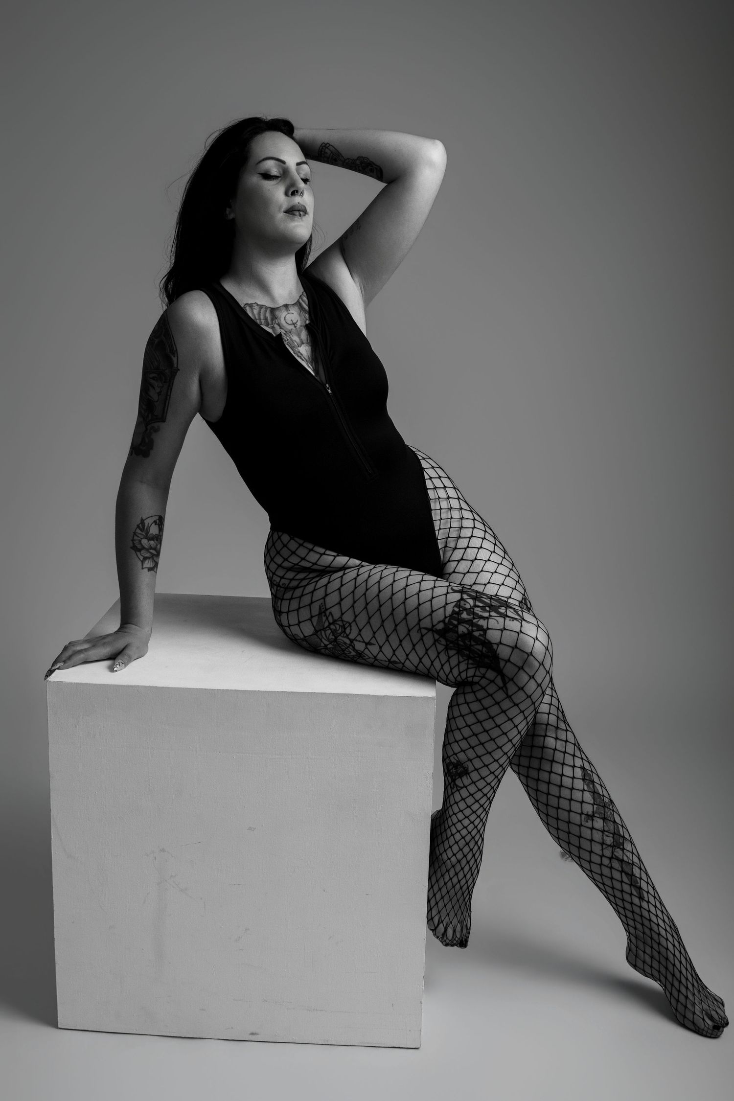 Femme en noir et blanc assise sur un cube avec des collants résille, portrait boudoir - Cindy Poulet photographe