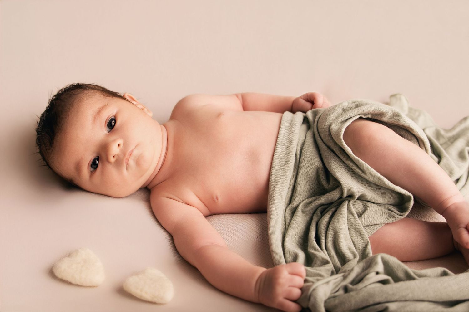 Portrait de nouveau-né par Cindy Poulet Photographe : séance naissance avec un bébé éveillé sur fond beige, drapé d'un tissu vert sauge et p