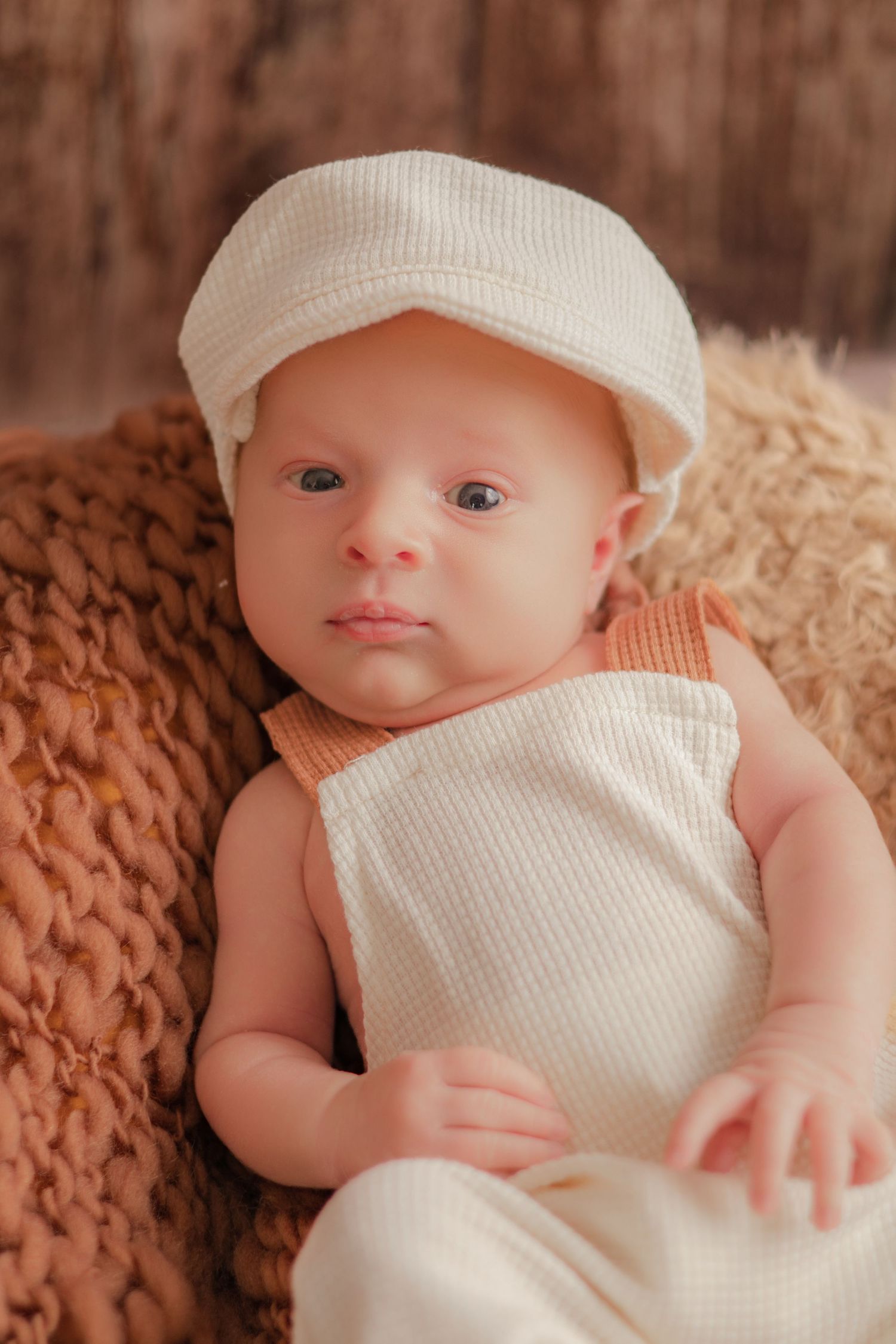 Portrait de nouveau-né par Cindy Poulet Photographe : bébé portant une petite casquette et une salopette blanche.