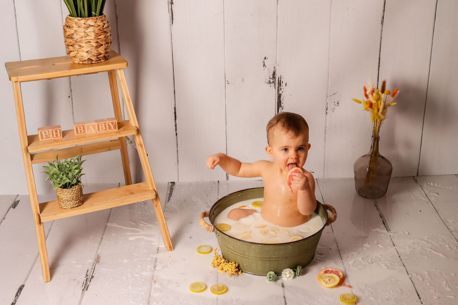 Décor de studio en bois avec bébé s'amusant dans un bain de lait aux agrumes, photographie de naissance originale par Cindy Poulet