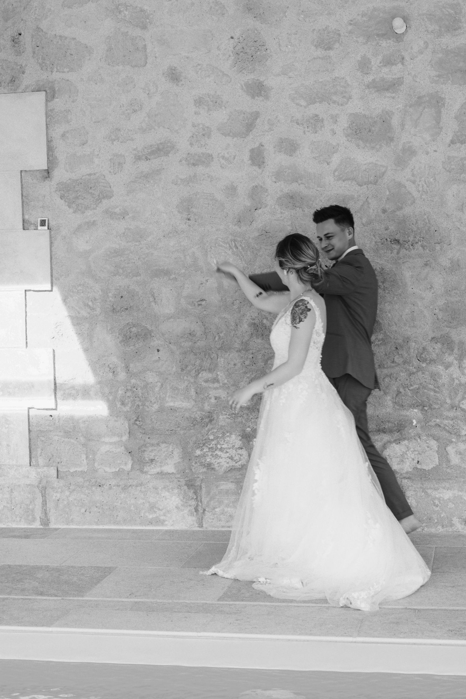 Couple de mariés en noir et blanc devant un mur en pierre, photo de mariage