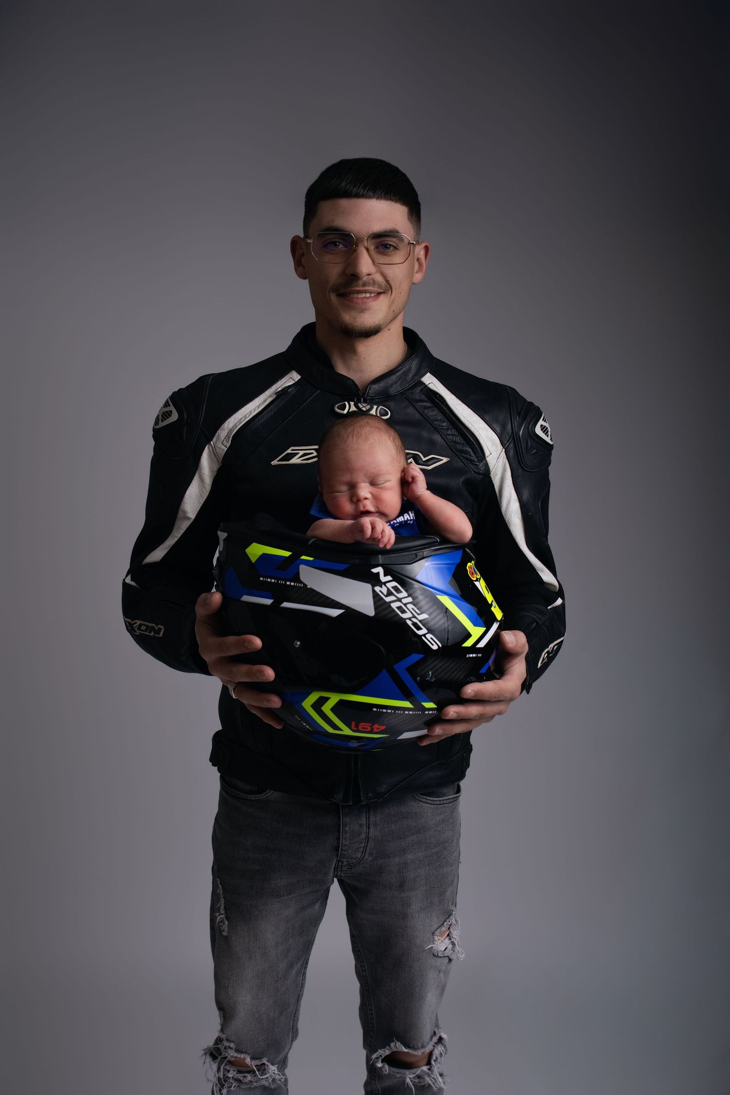 Père en veste de moto tenant son nouveau-né dans son casque, portrait naissance original - Cindy Poulet photographe
