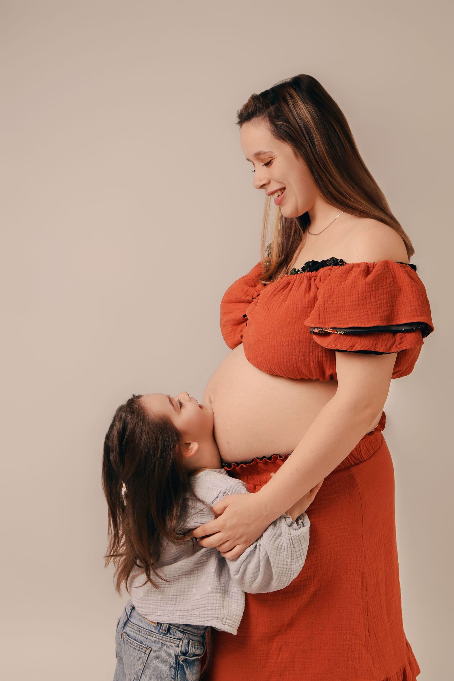 Petite fille embrassant le ventre de sa maman enceinte en studio, shooting photo maternité et famille par Cindy Poulet Photographe