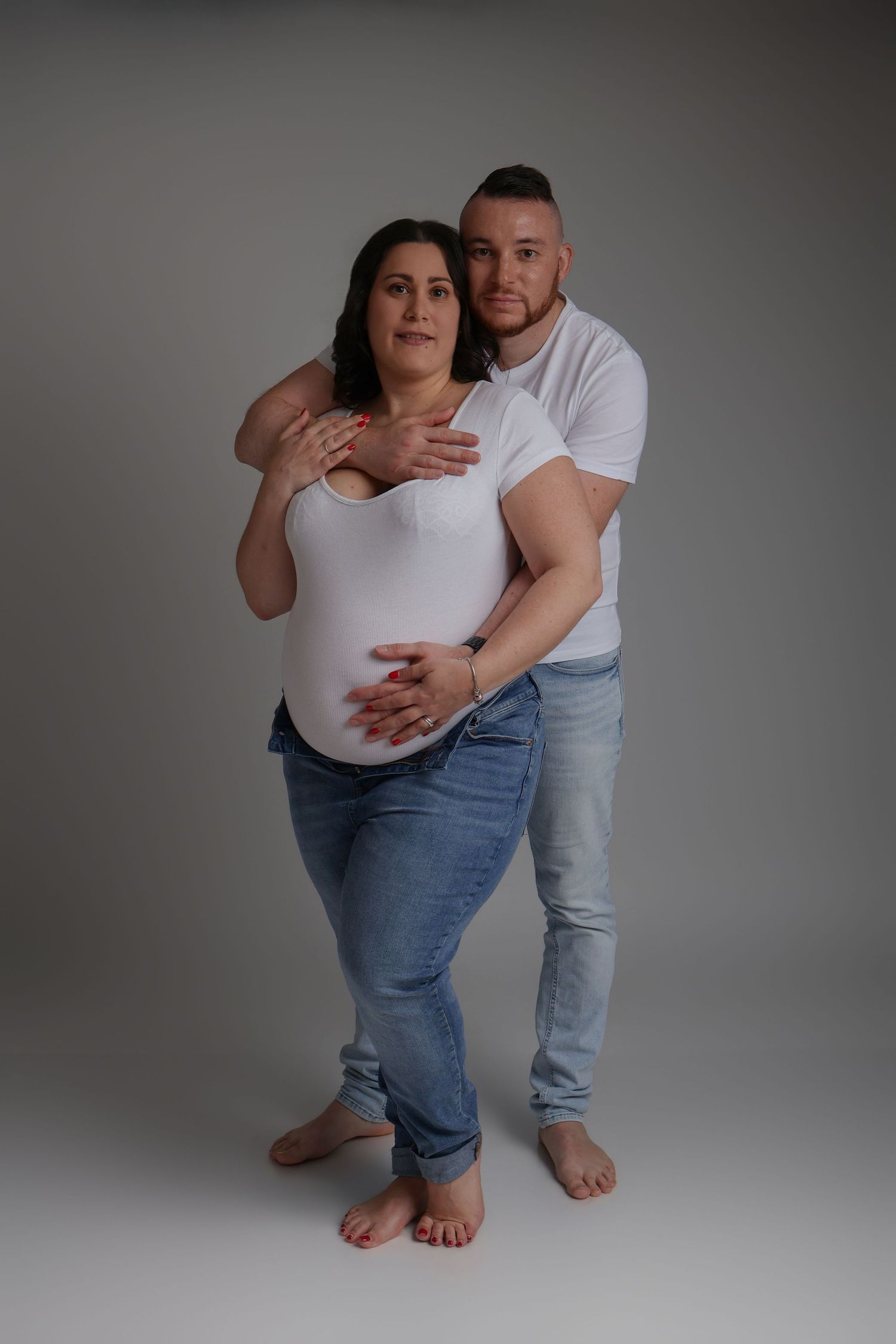 Couple enceinte en studio, femme en blanc, séance grossesse