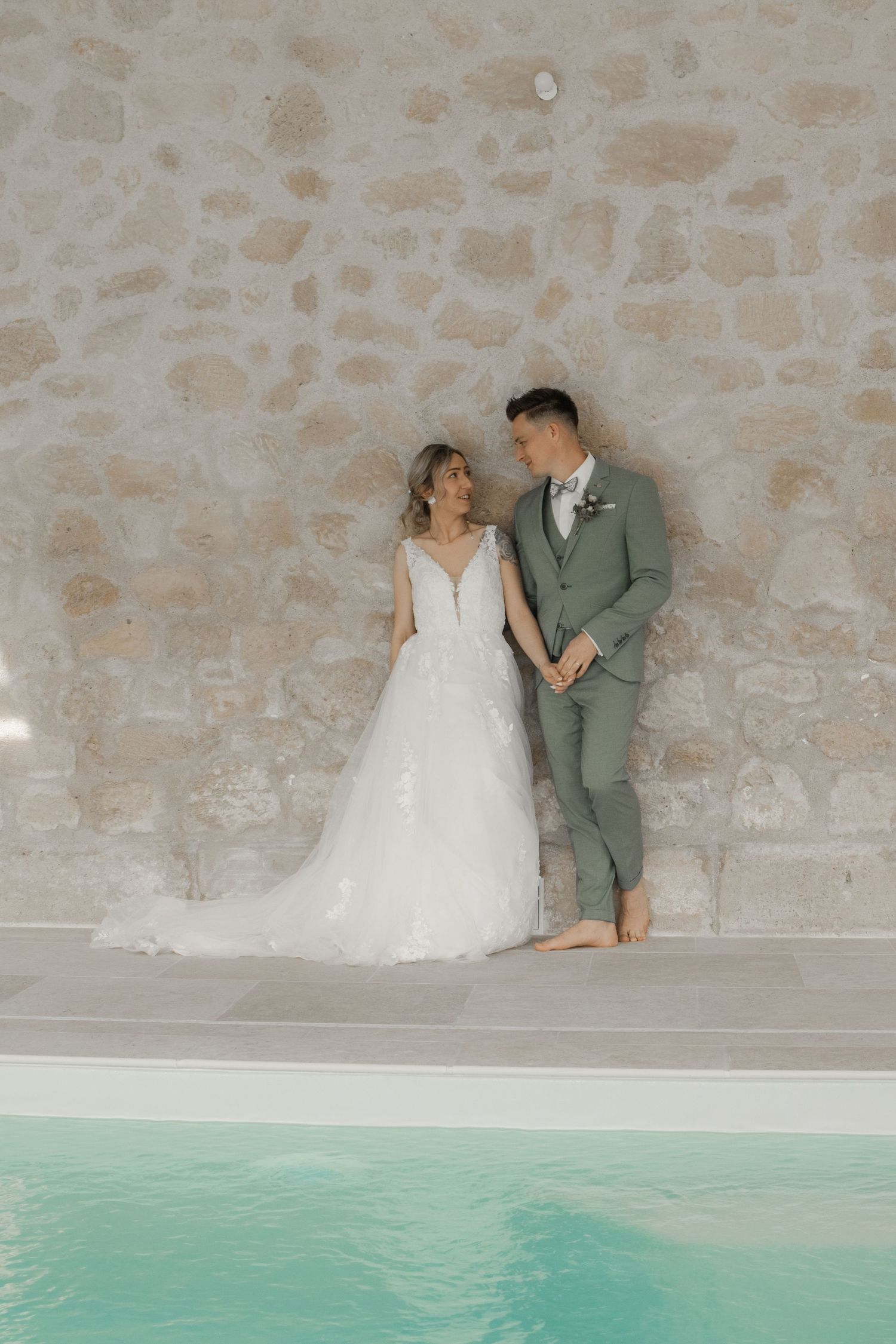 Couple de mariés debout au bord d'une piscine devant un mur en pierre, photo de mariage