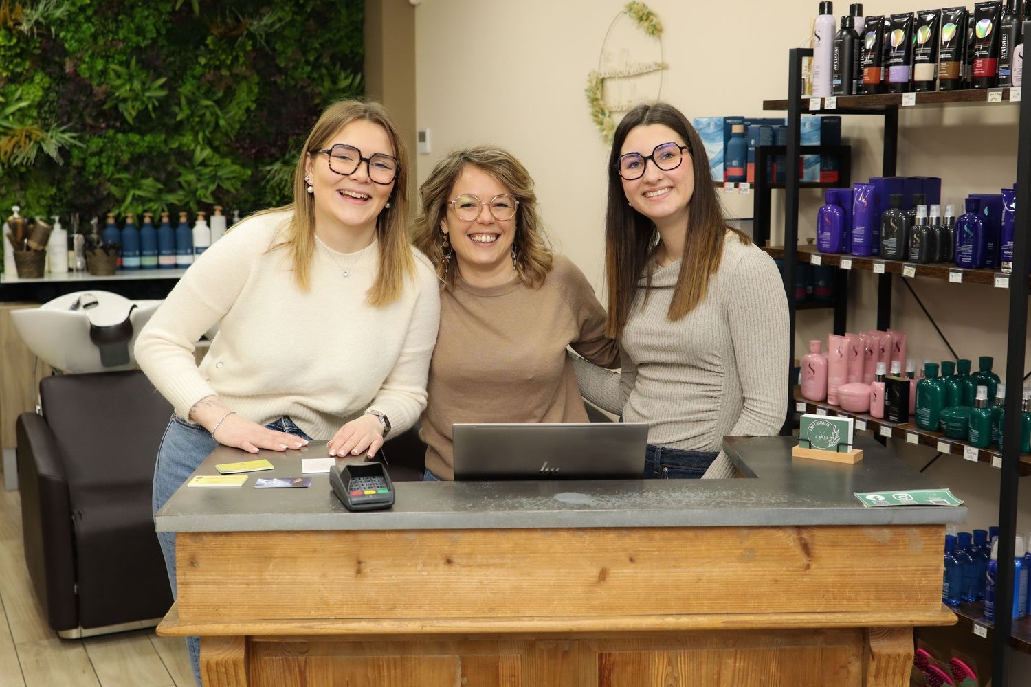 Portrait d'équipe par Cindy Poulet Photographe : trois coiffeuses souriantes derrière le comptoir d'un salon de coiffure moderne.