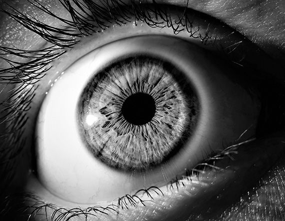 Close-up black and white macro photo of a human eye showing detailed iris texture and pupil.