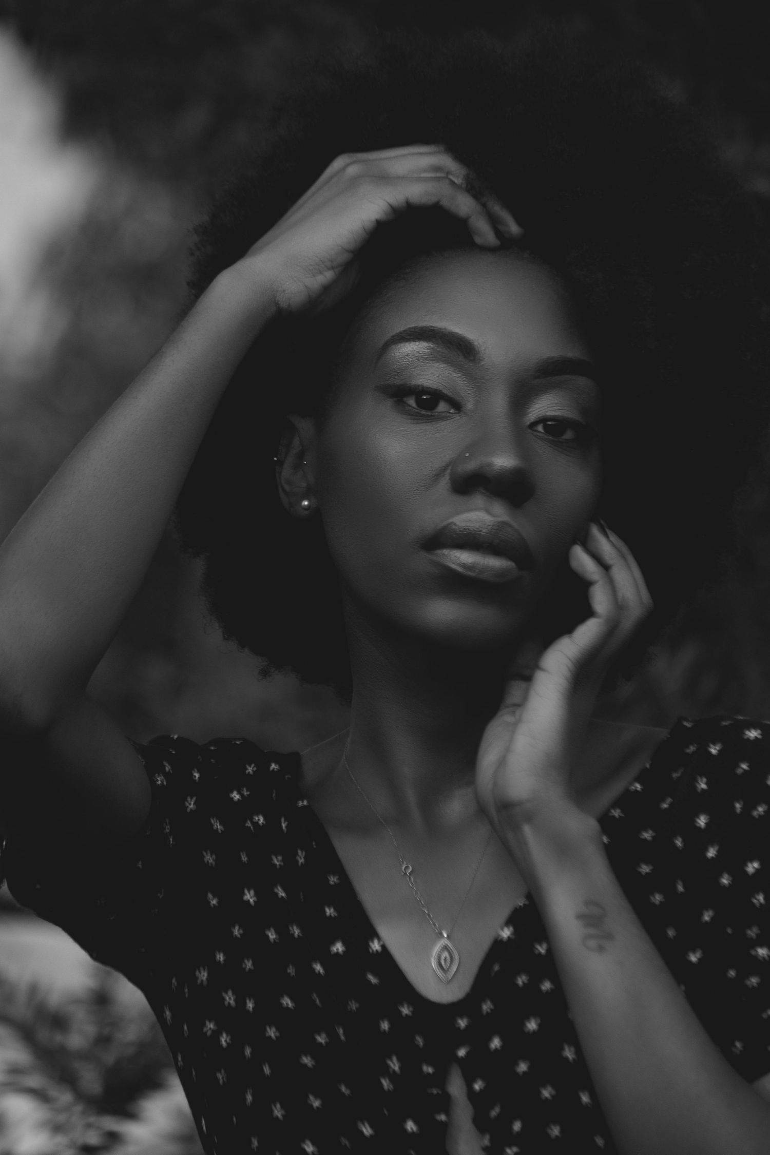 Black and white portrait of a young Black woman in a floral dress, posing thoughtfully with hands near her face.