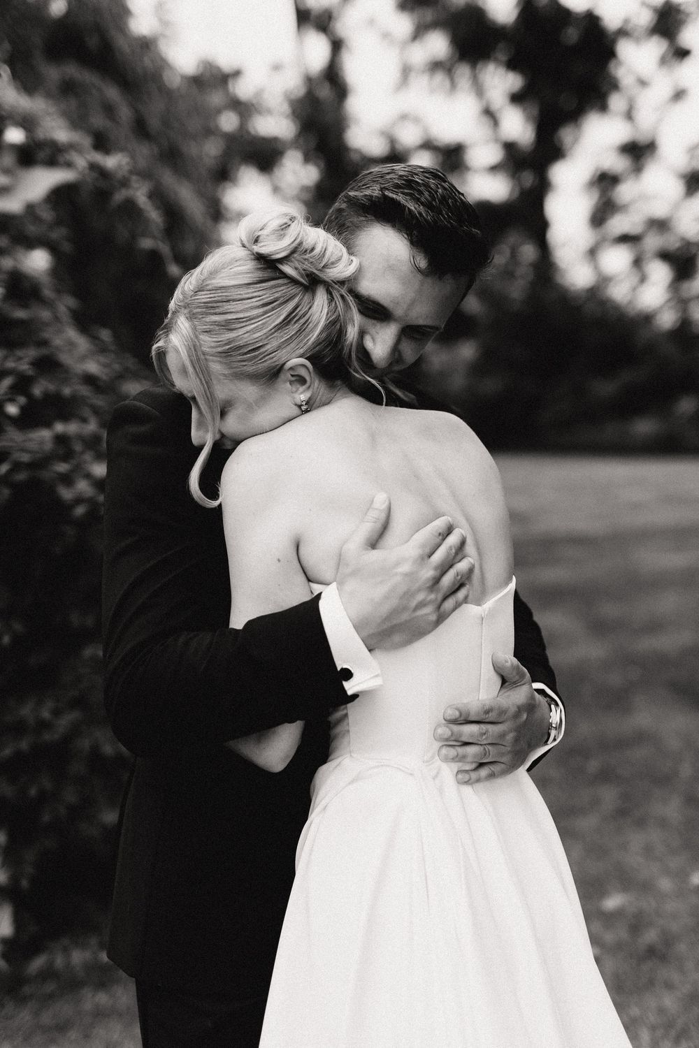 Black and white photo of a bride and groom sharing an emotional embrace outdoors on their wedding day.