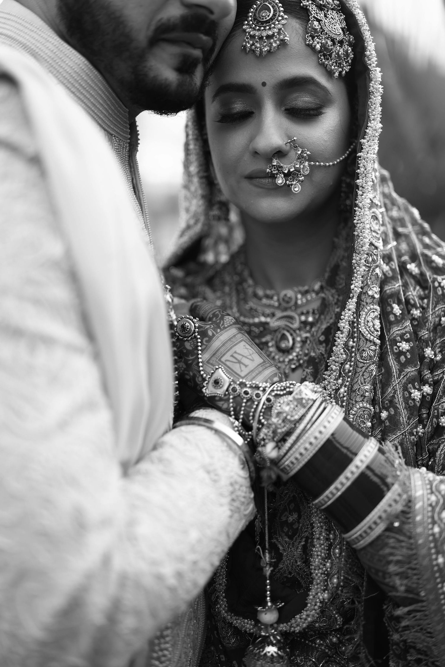 Black and white photo of an Indian bride in traditional bridal jewelry and dupatta with groom during wedding ceremony.