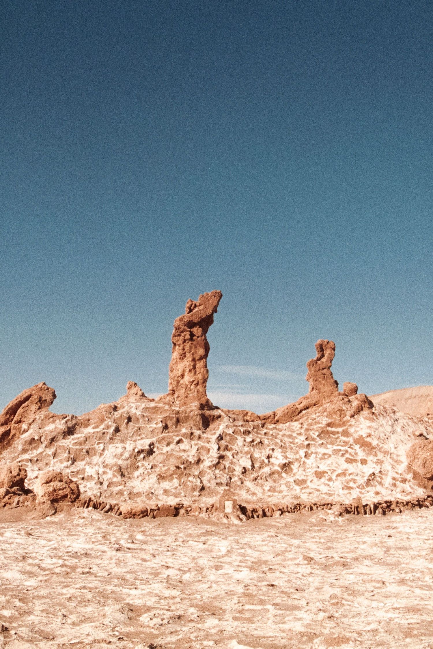 Towering red rock formations rise against a clear blue sky in the arid Atacama Desert, Chile.