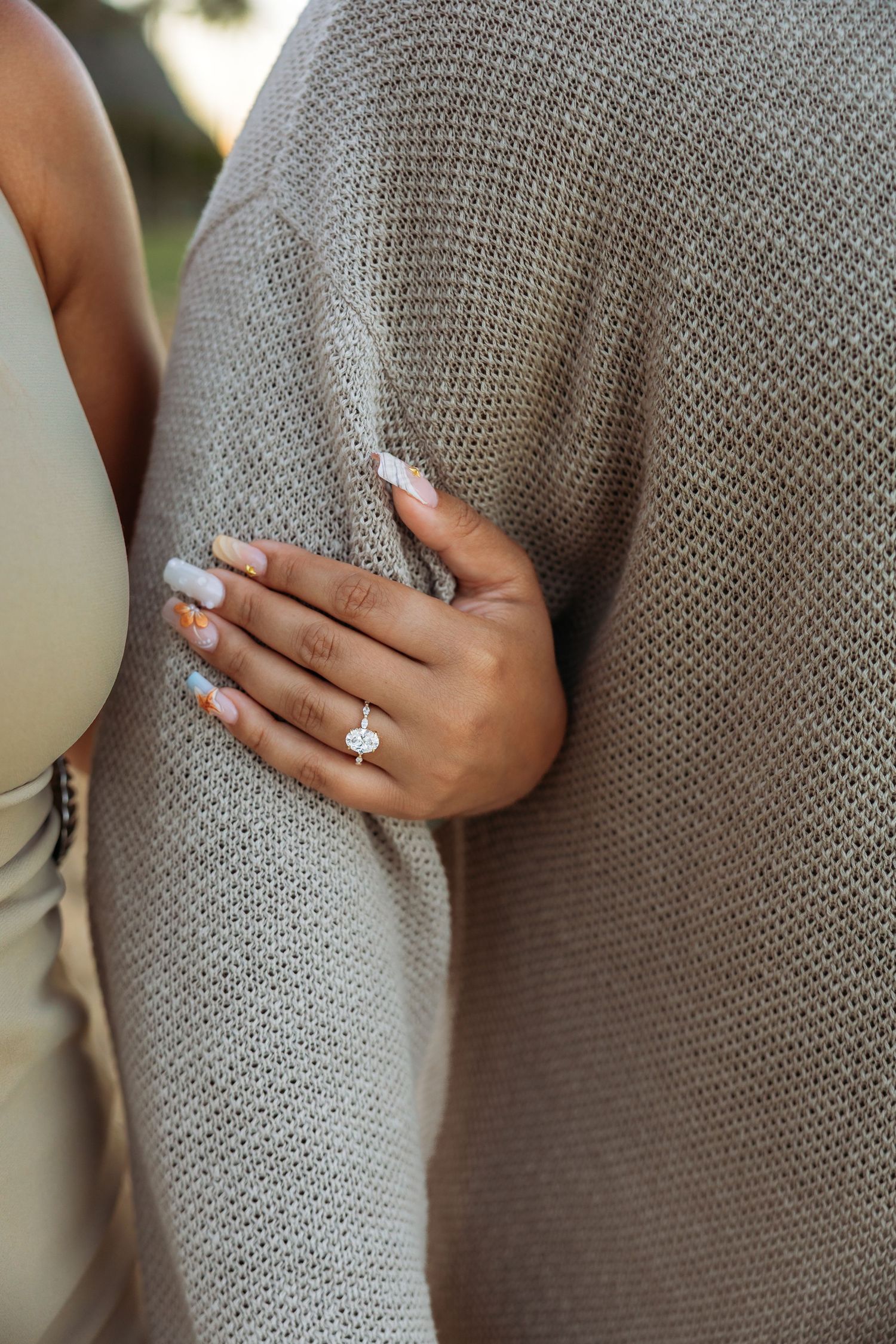 Close-up of woman's hand with oval diamond engagement ring resting on man's gray knit sweater.