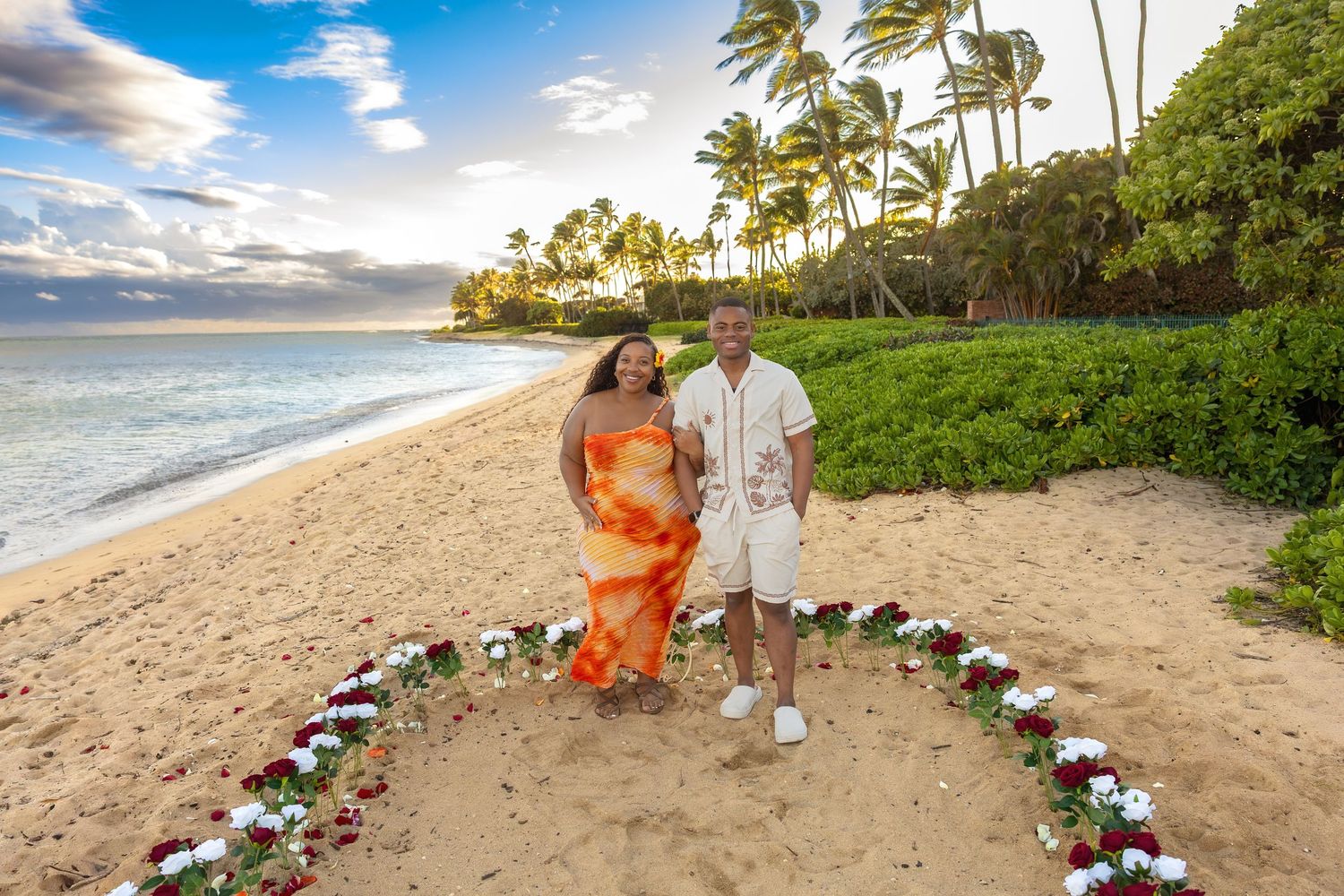 Newly engaged couple standing inside heart-shaped floral arrangement on tropical Hawaiian beach.
