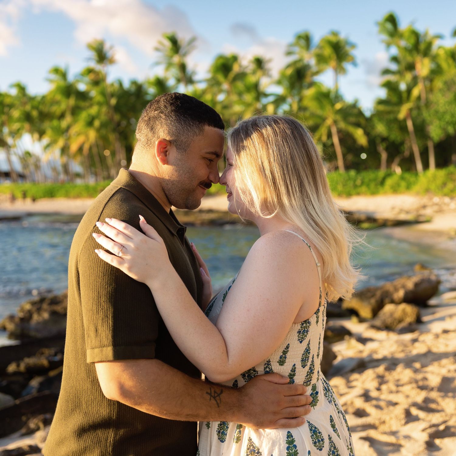 Couple sharing a romantic moment on a tropical beach with palm trees and golden sunset light.
