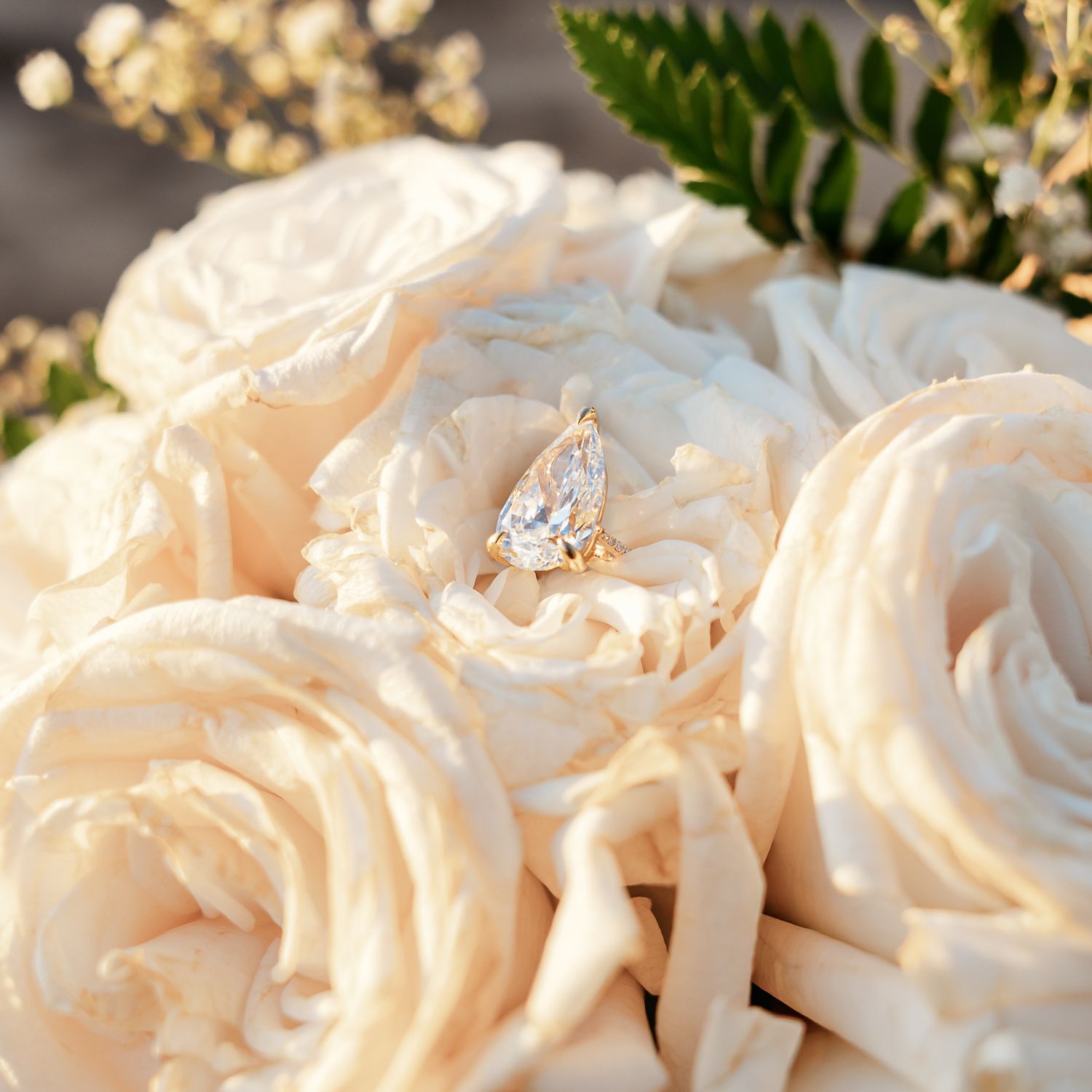 Elegant pear-shaped diamond engagement ring nestled among cream roses in bridal bouquet.