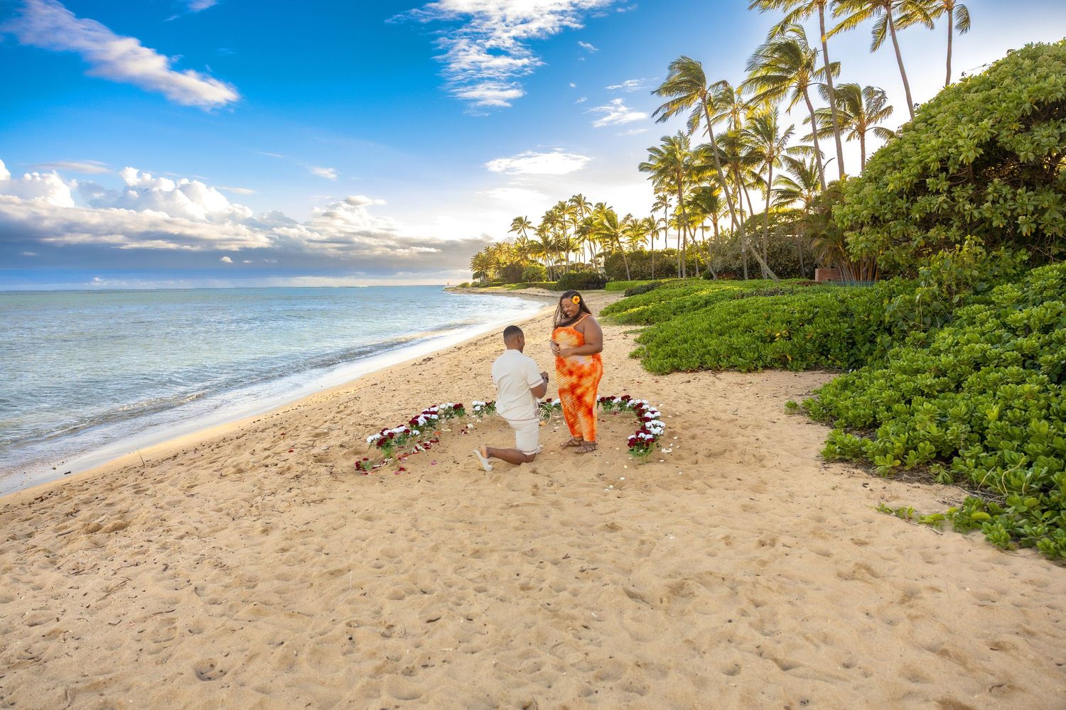 Romantic beach proposal on Maui with couple surrounded by floral decorations at sunset.