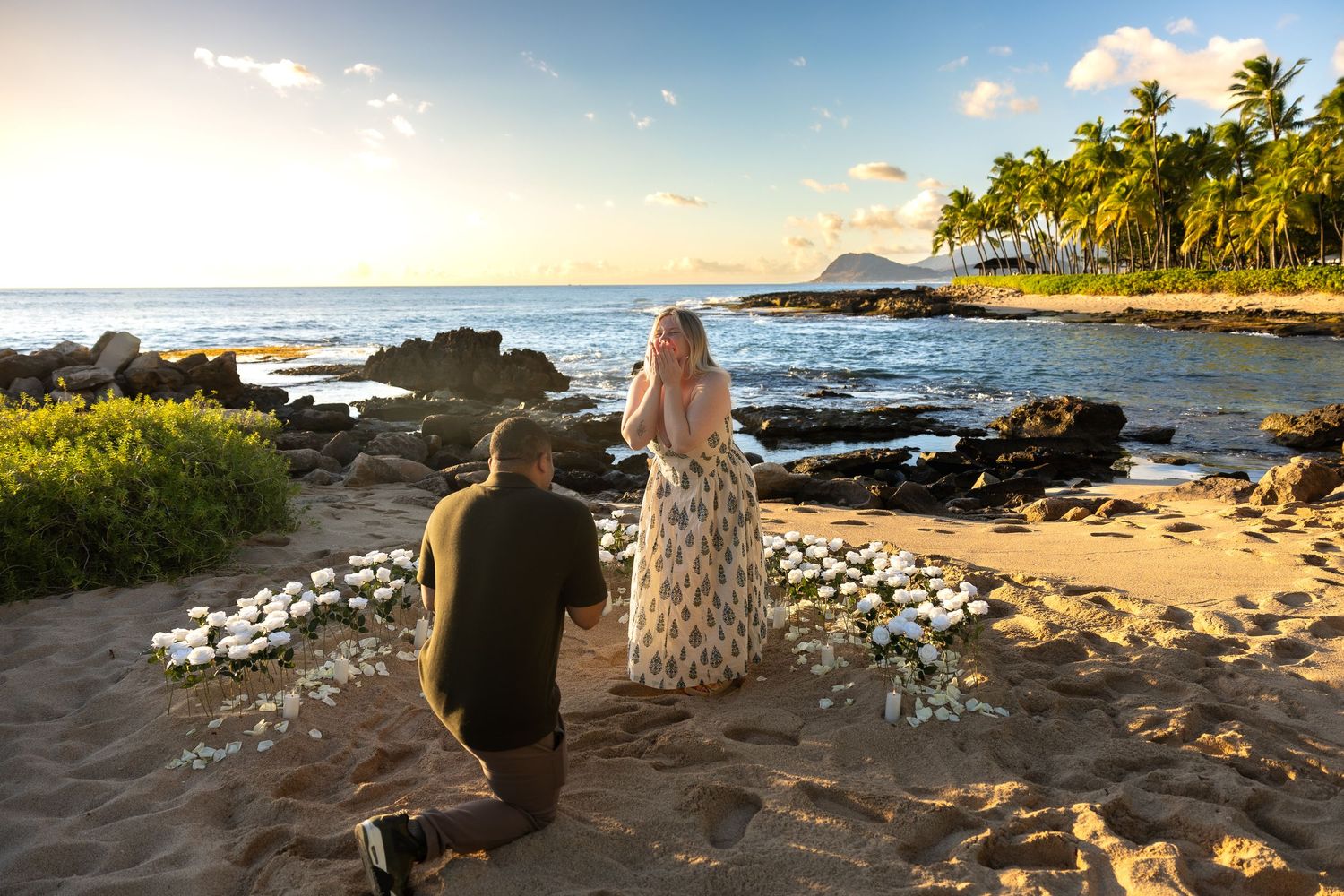 Emotional beach marriage proposal at sunset with white flower arrangement and tropical ocean backdrop in Hawaii.