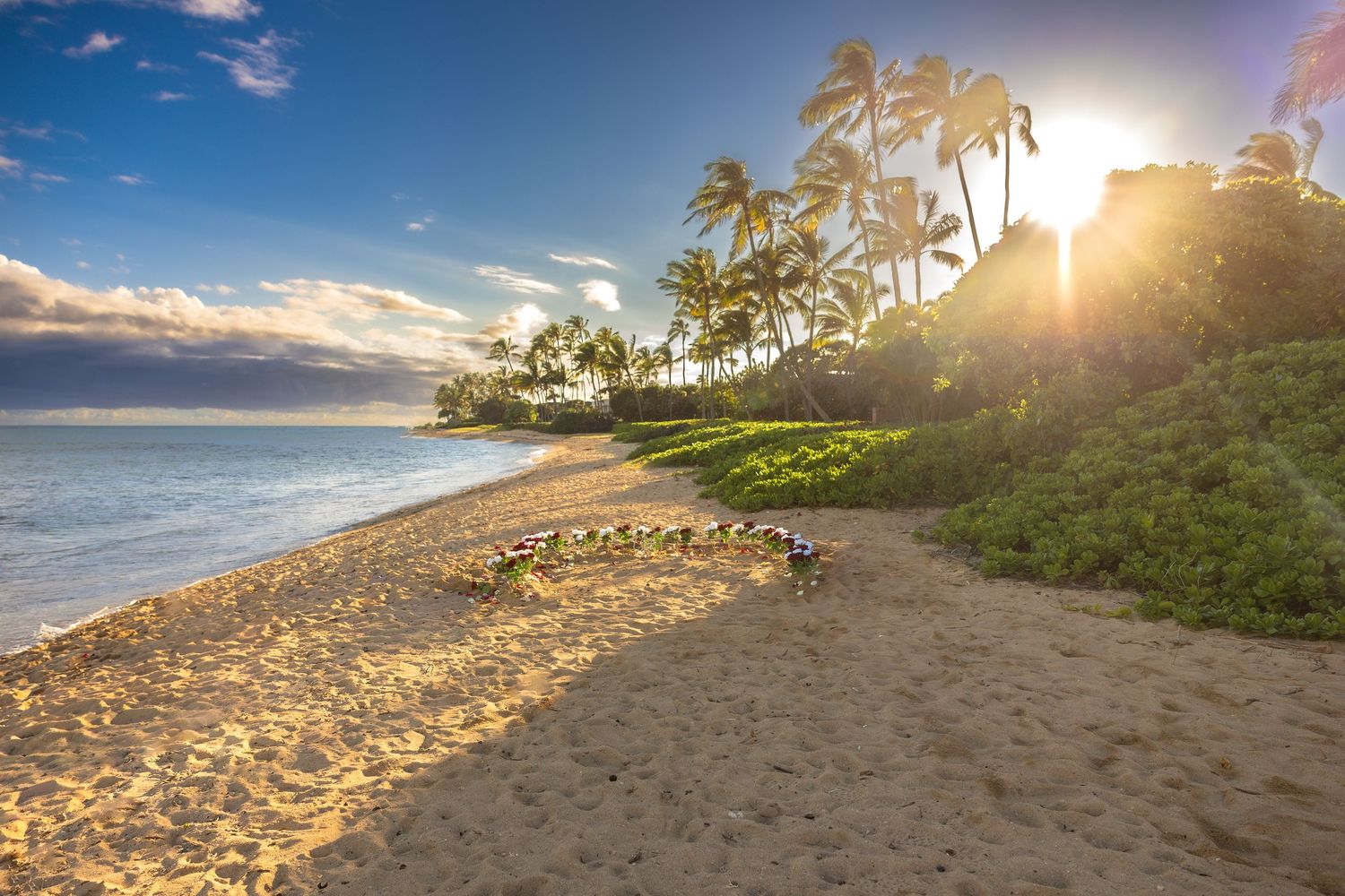 Stunning Hawaiian beach sunset with heart-shaped flower arrangement on golden sand.