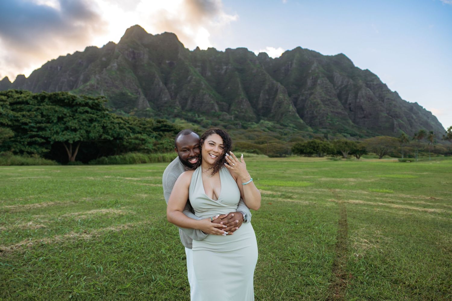 Happy couple embracing on green lawn with stunning Ko'olau mountain range behind them.