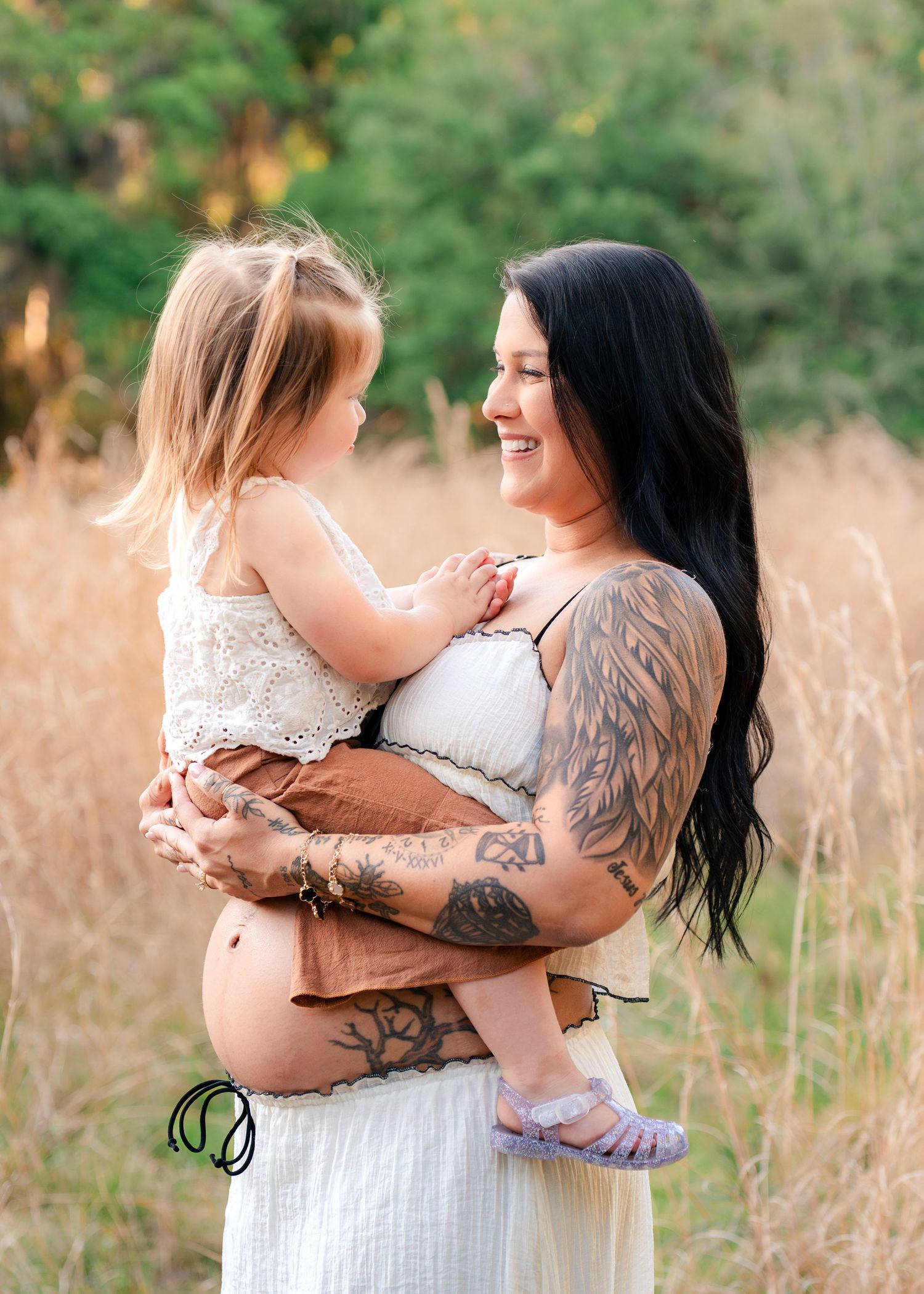 Expecting mother holding daughter during maternity session in the golden grass of Lake Runnymede Conservation Area in St Cloud Florida