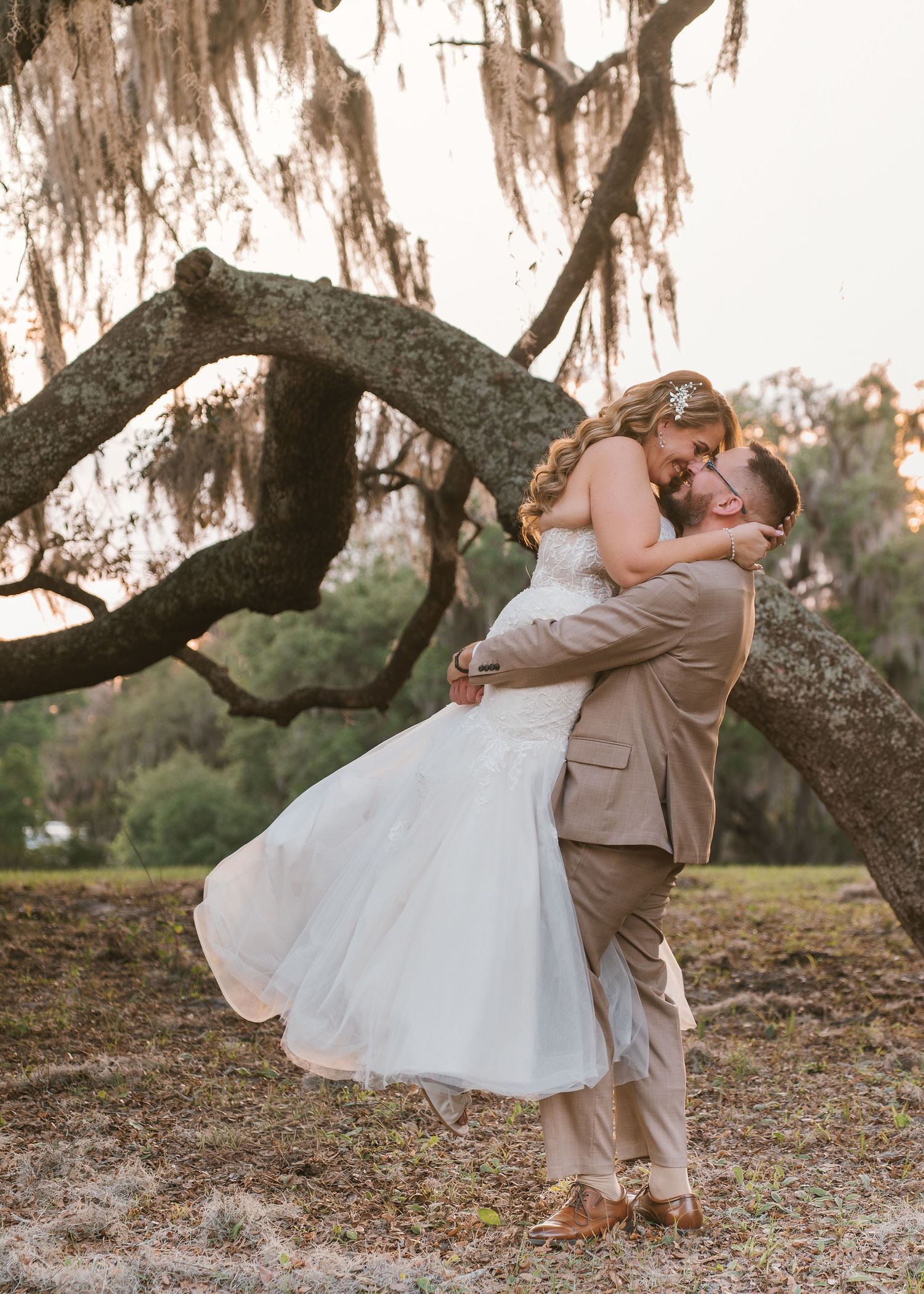 Joyful newlywed portraits with the groom lifting the bride beneath the moss-covered oak trees at Moss Estates wedding venue in Eustis