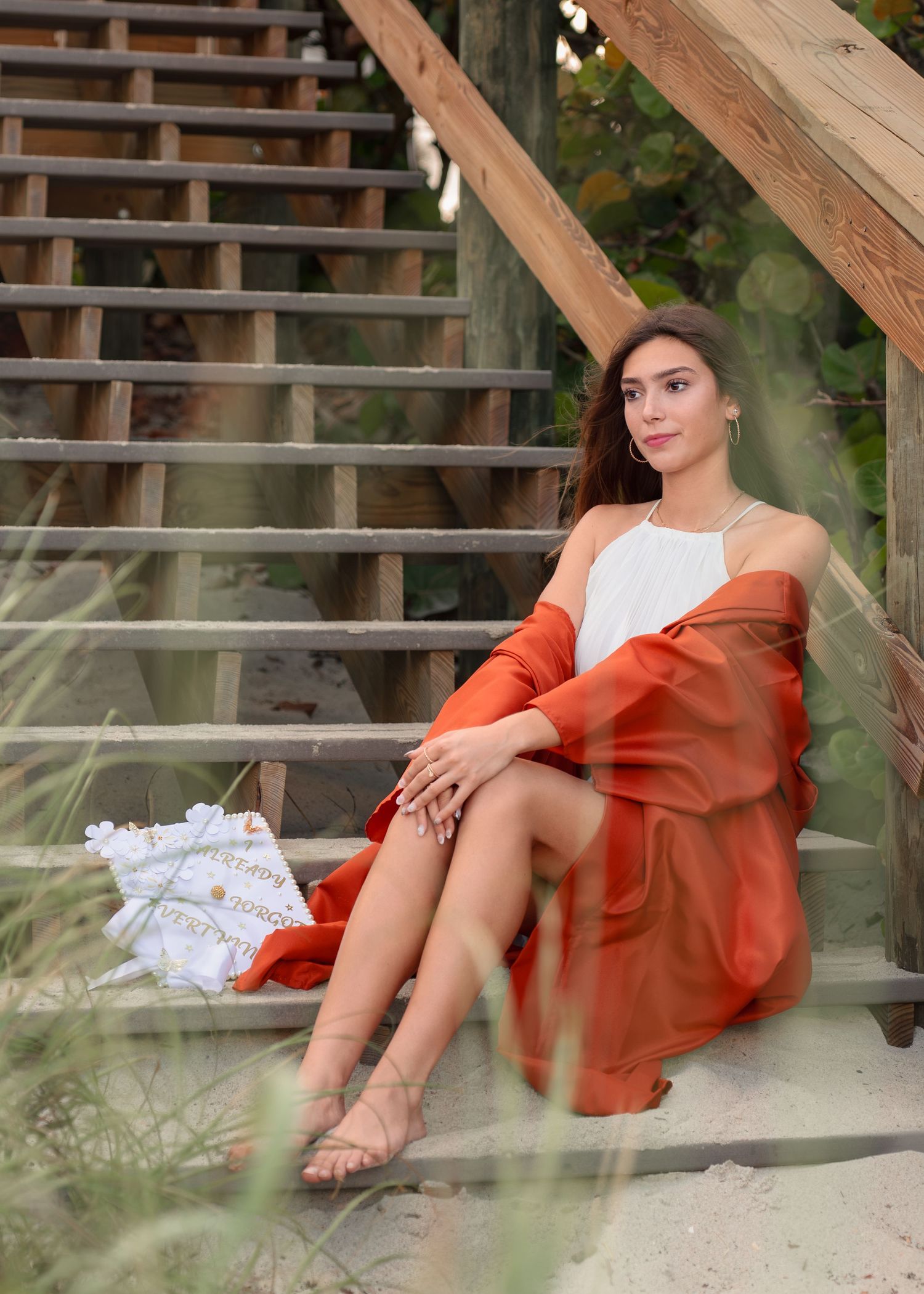Stunning graduation portrait photography featuring the sandy shoreline and golden sunset at Melbourne Beach with cap and gown.