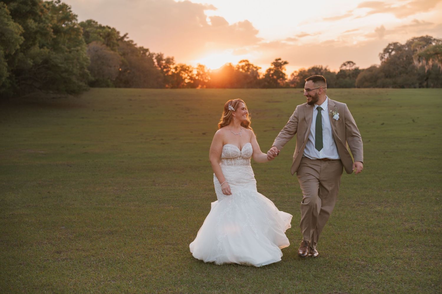 Bride and groom walking hand in hand through the open field during sunset at Moss Estates wedding venue in Eustis, Florida.
