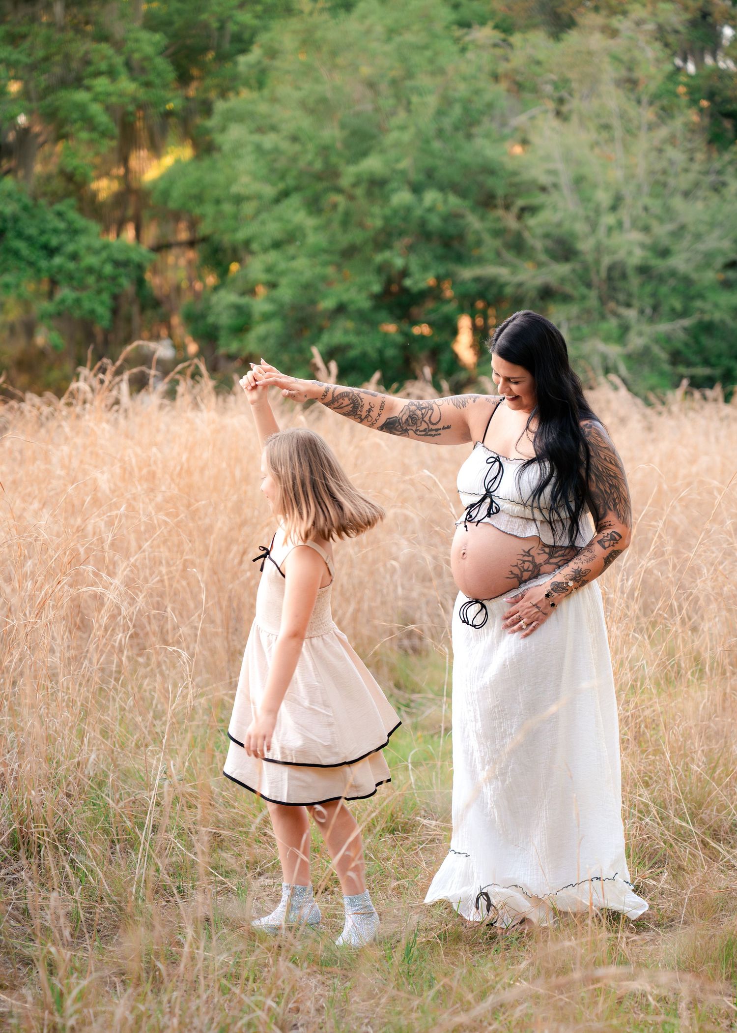Expecting mother twirling her daughter beneath in tall grass during maternity session at Lake Runnymede Conservation Area in St Cloud FL
