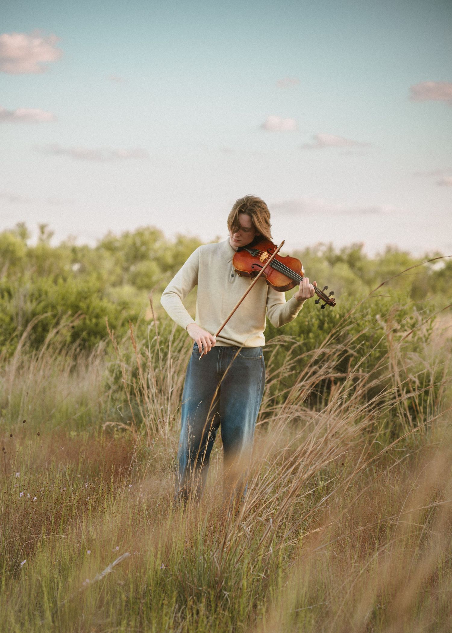 High school senior playing the violin against blue sky at graduation portrait session at Lake Runnymede Conservation Area St. Cloud Florida
