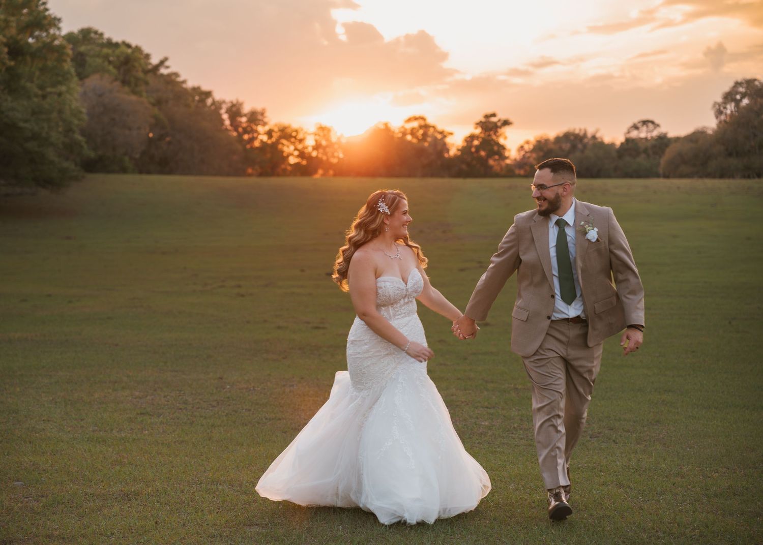 Bride and groom walking hand in hand through the open field during sunset at Moss Estates wedding venue in Eustis, Florida.